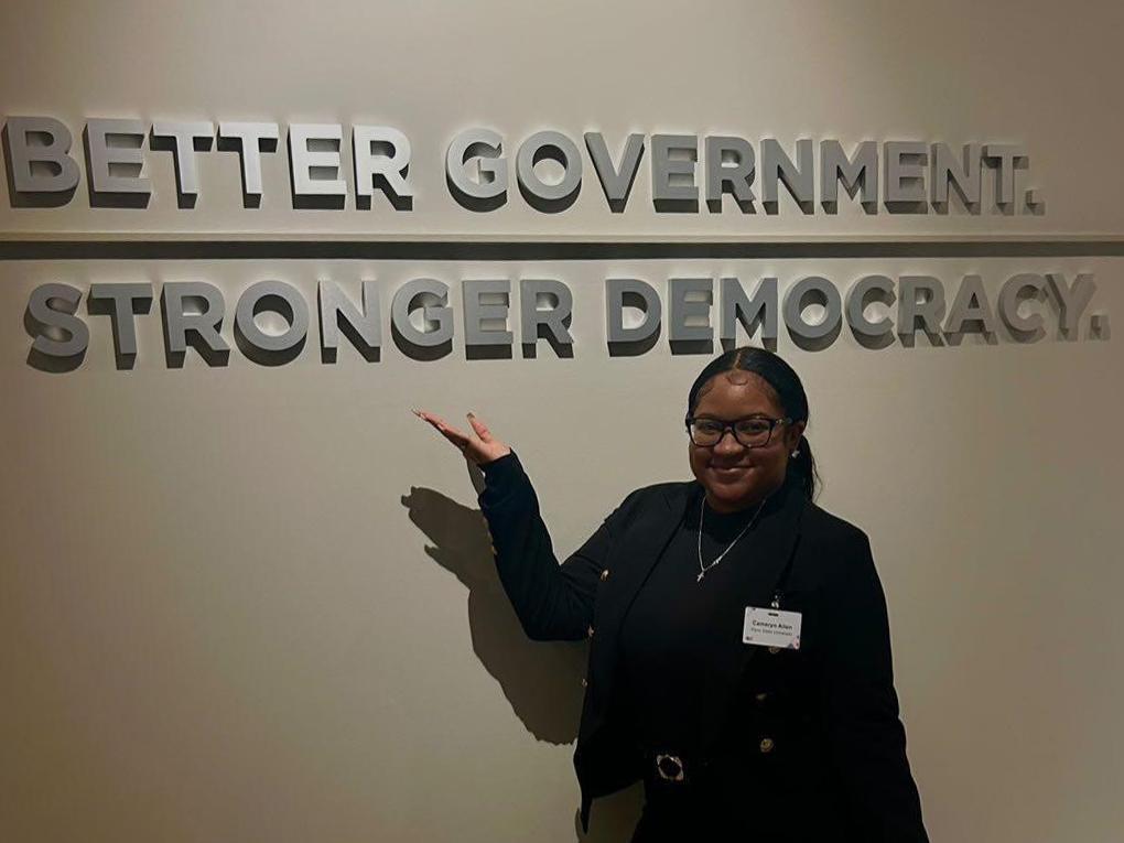 Penn State student Cameryn Allen stands in front of a sign that reads “Better government. Stronger democracy.” at the “D.C. Trek” sponsored by the Liberal Arts Career Enrichment Network.