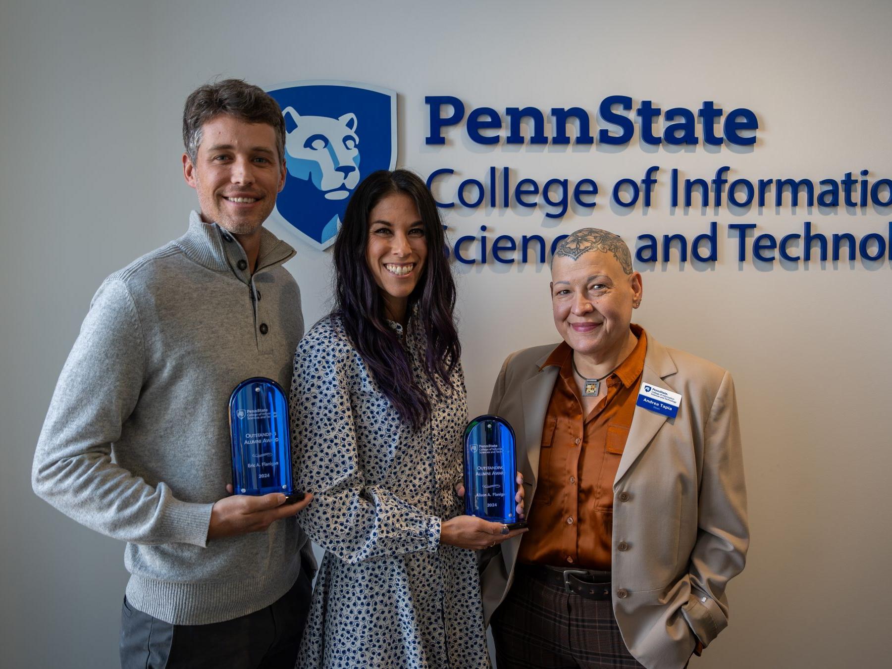 three people display awards in front of college seal