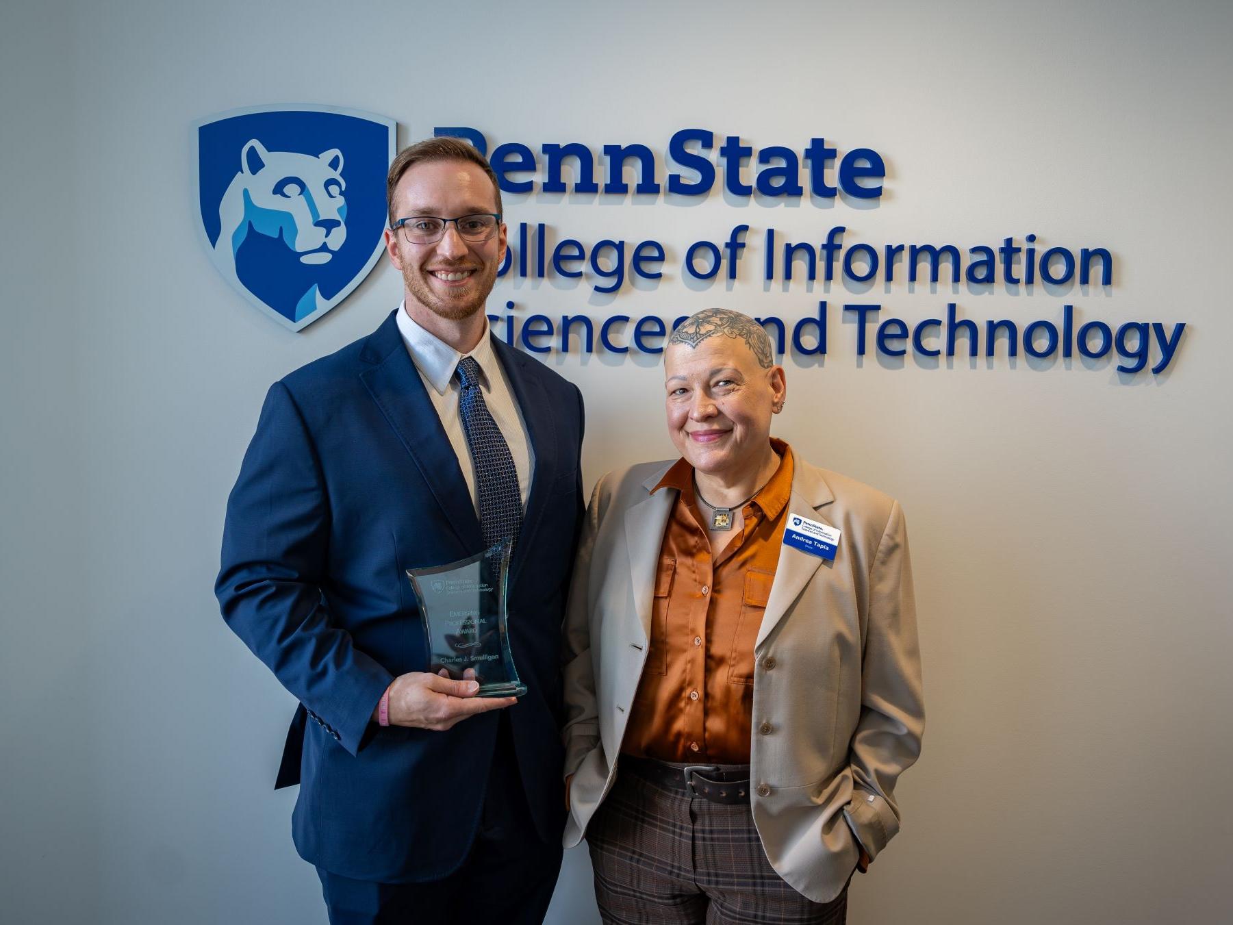 two people in business attire display award in front of college seal