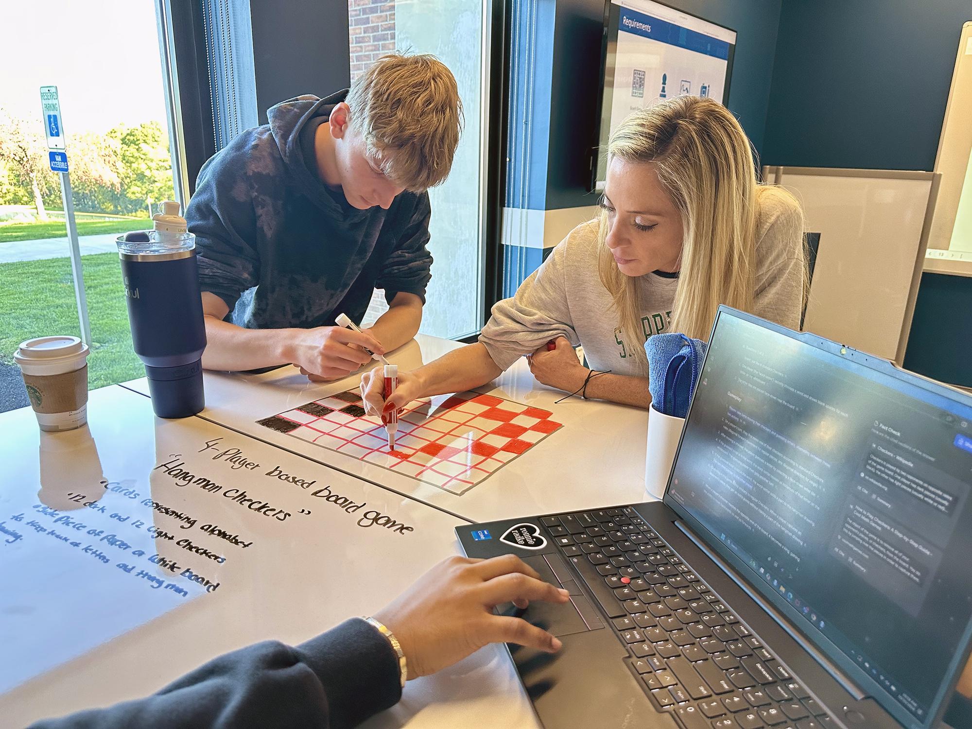 Two students sit at a table and work on a board game they designed