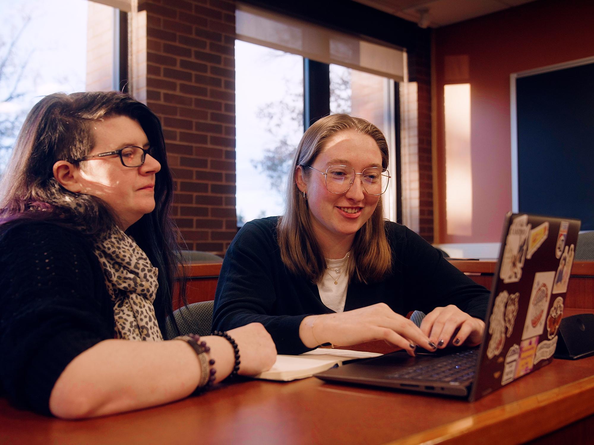 Maddie Hindman (right) and Kelly Duran (left), lecturer of public policy, sit at a desk in a classroom while looking at a laptop.