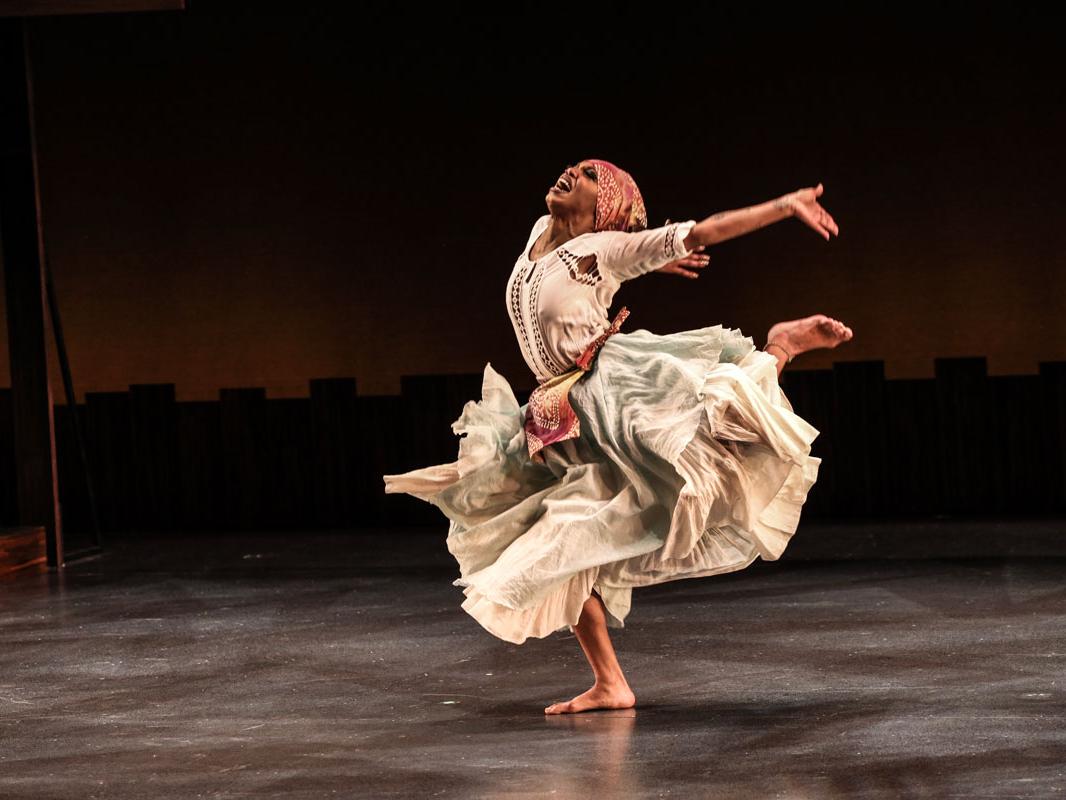 A Black dancers throws her arms back and kicks one leg high behind her.