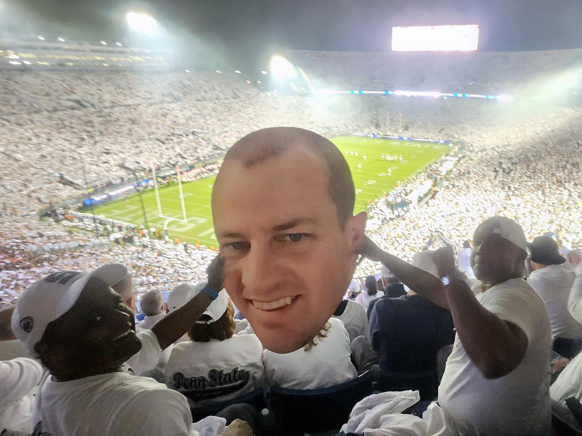 Two men pose inside Beaver Stadium with a printed cutout of a man's head.
