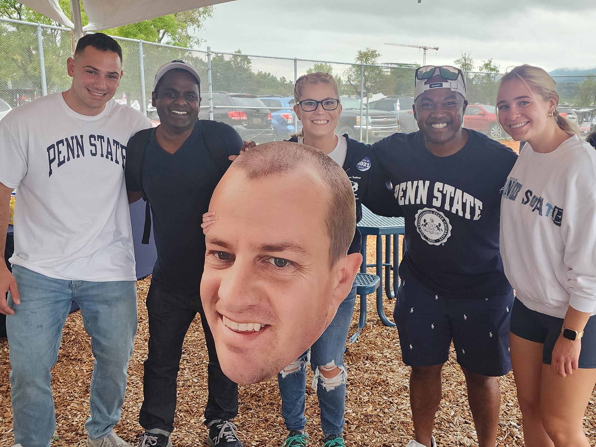 A group of people pose for a photo with a large cutout of a man's face.