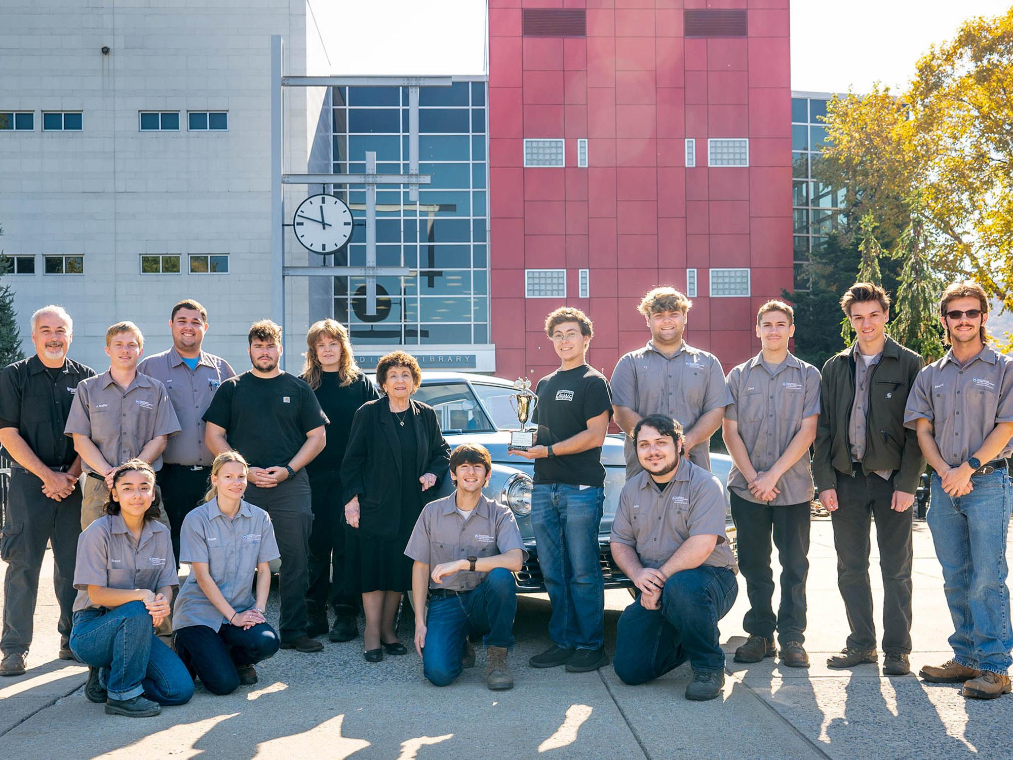 A group of students pose for a photo outside with a car