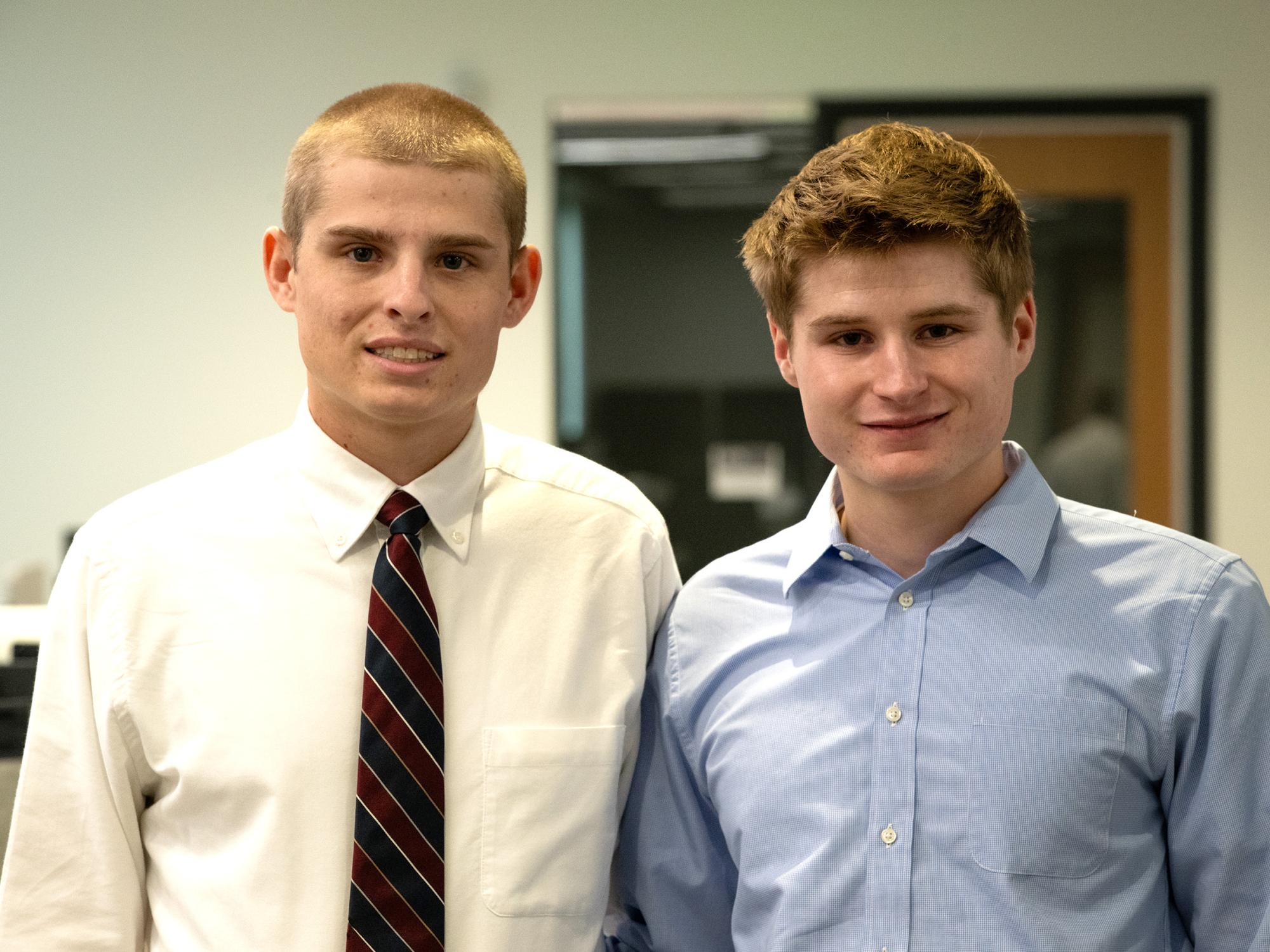 Two students wearing professional attire pose indoors.