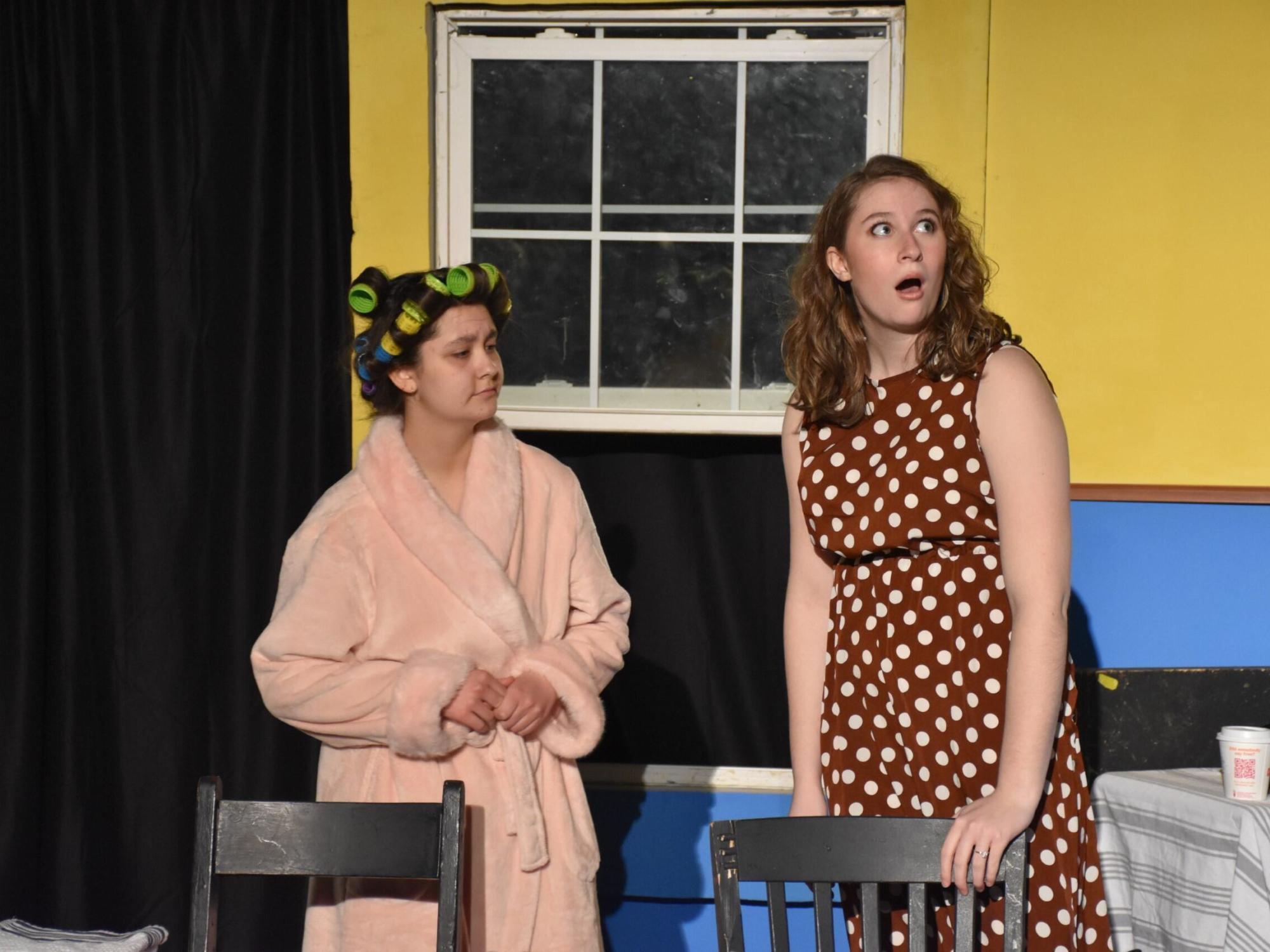 two students on stage one in bathrobe and one in polka dot dress