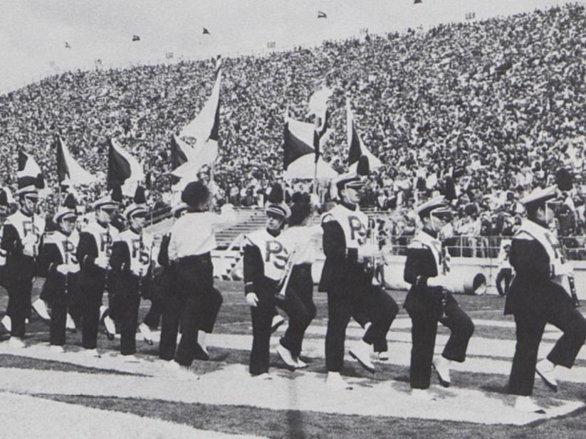 Musicians and color guard members march on a football field