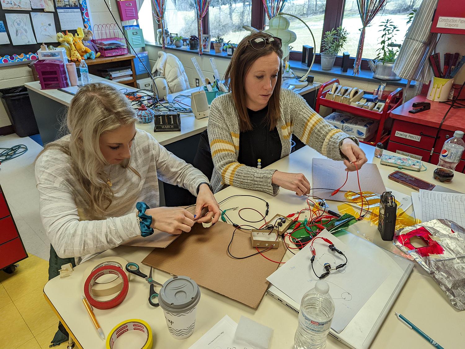 Two teachers sit at a table and work on a project.