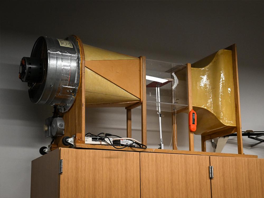A shiny glass and linoleum model wind tunnel is seen on a shelf above a lab cabinet.   