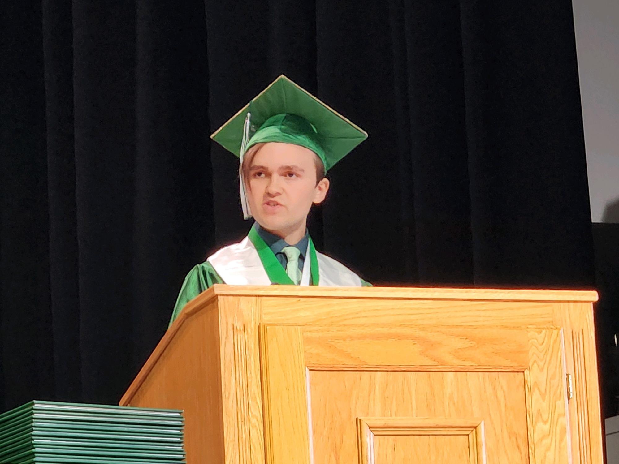 Gwynne Morris gives the valedictorian speech behind a podium while wearing a green and white cap and gown at her high school graduation this past June.