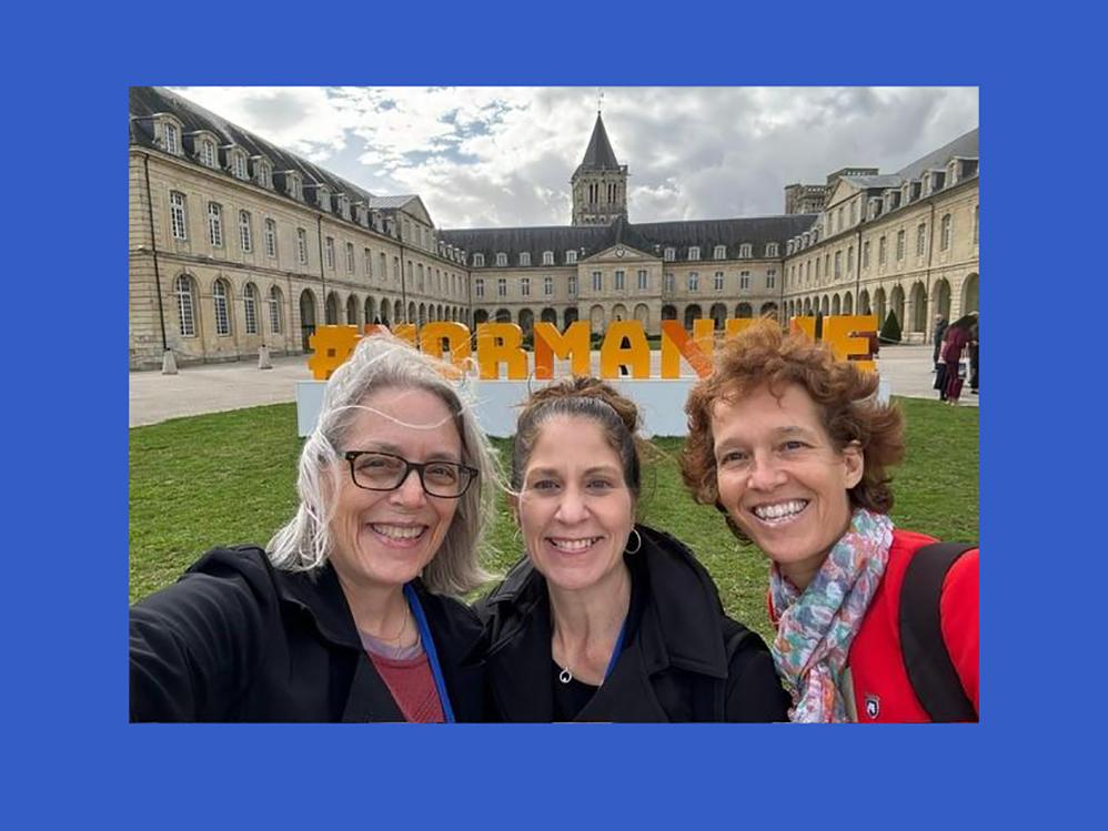 A group of three women smiling in front of an old building