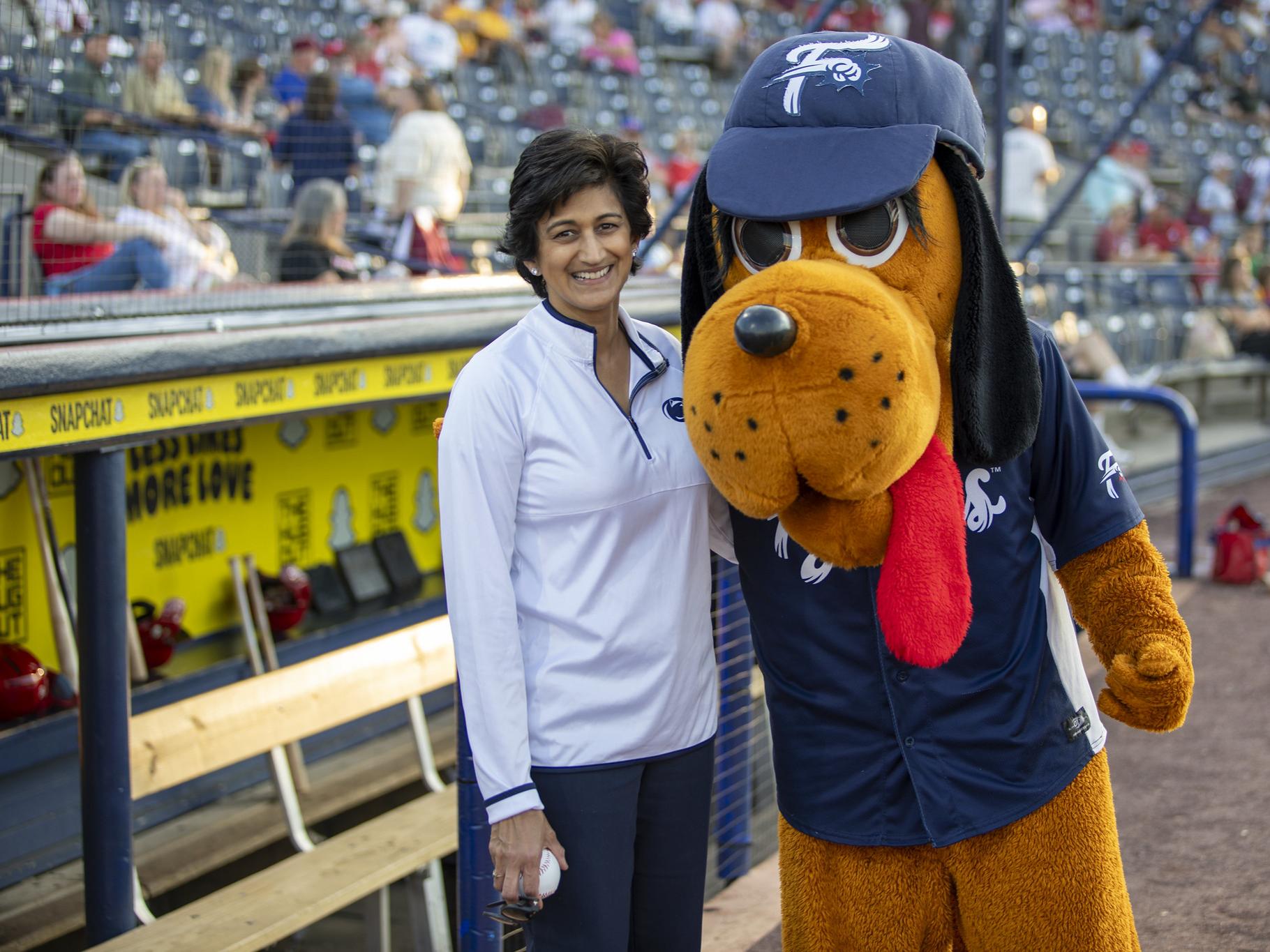 Chancellor Pyati holds a baseball while posing with a hound dog baseball mascot