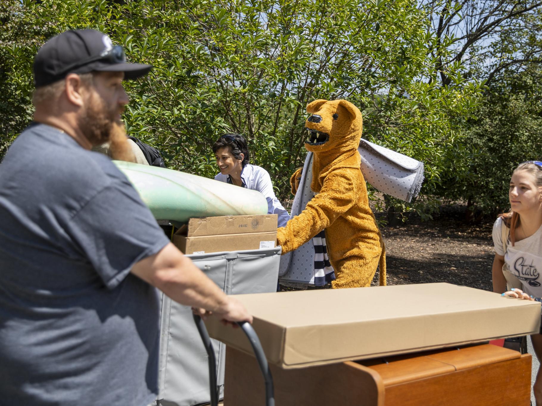 A parent, student, Chancellor Pyati and the Nittany Lion mascot move items into the residence halls