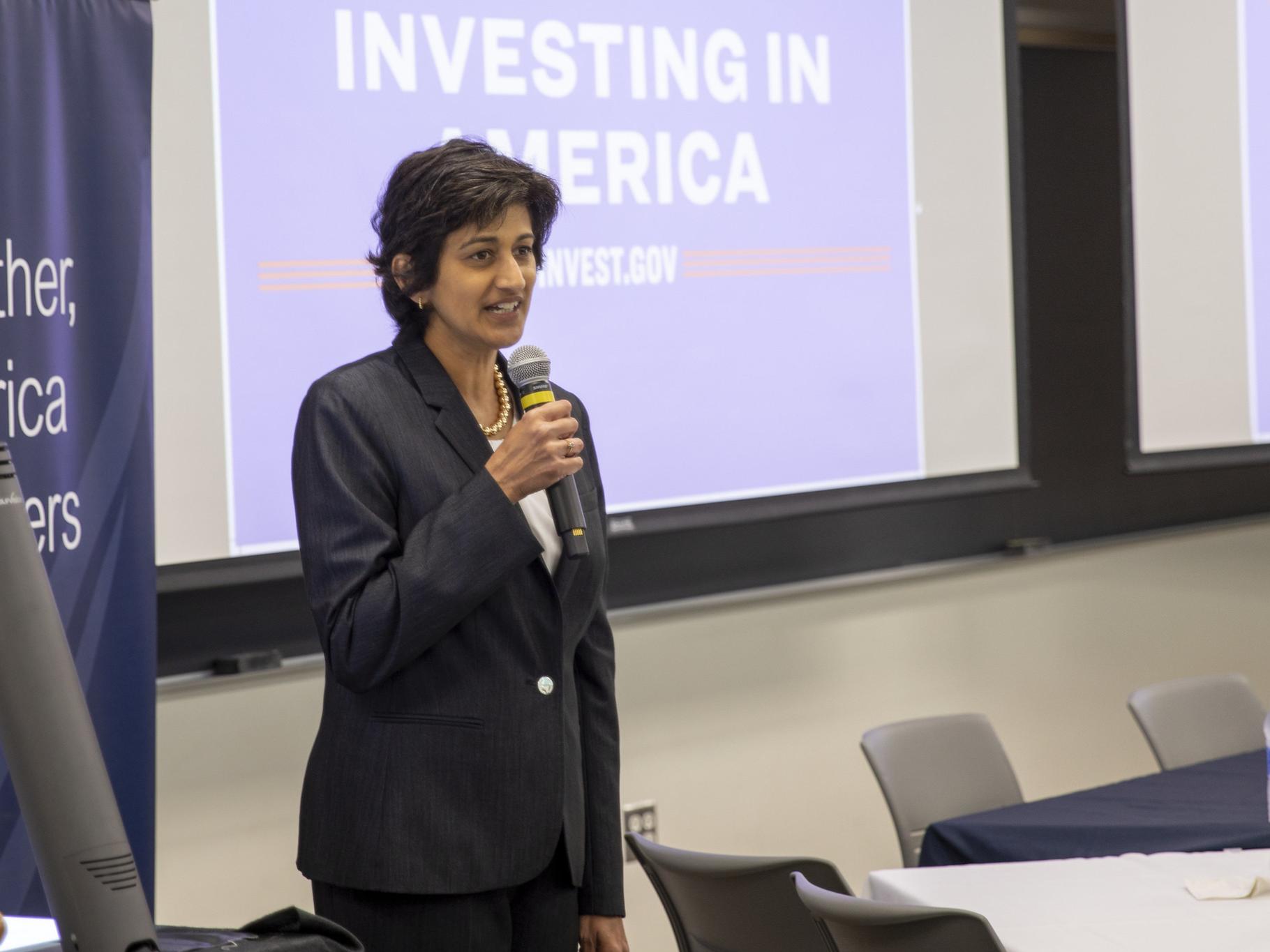 Chancellor Pyati holds microphone in front of signage reading "Investing in America"
