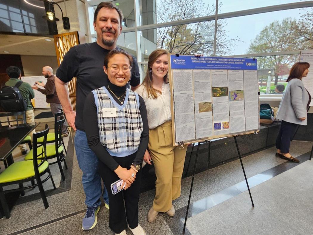 Two women and one man in front of a research poster. 
