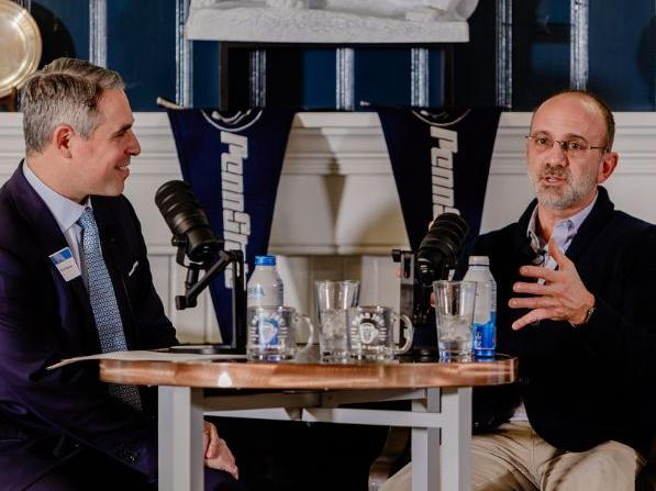 Photo of Ryan Newman and Gary Brandeis sitting at a high top table with podcast microphones recording the Dare to Disrupt Podcast live