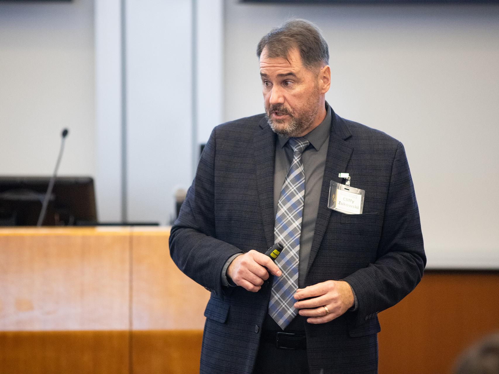 Cliffy Zukowski, in a suit, explains to a room full of people.