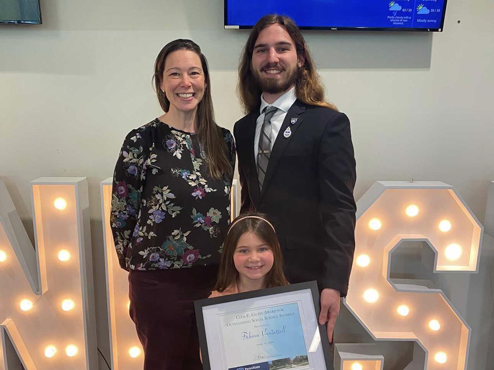 Fabian Vantassell poses with a professor and his little sister, who holds an award he received