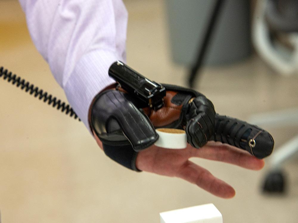 A hand in a glove-like device lifts a small circular object.