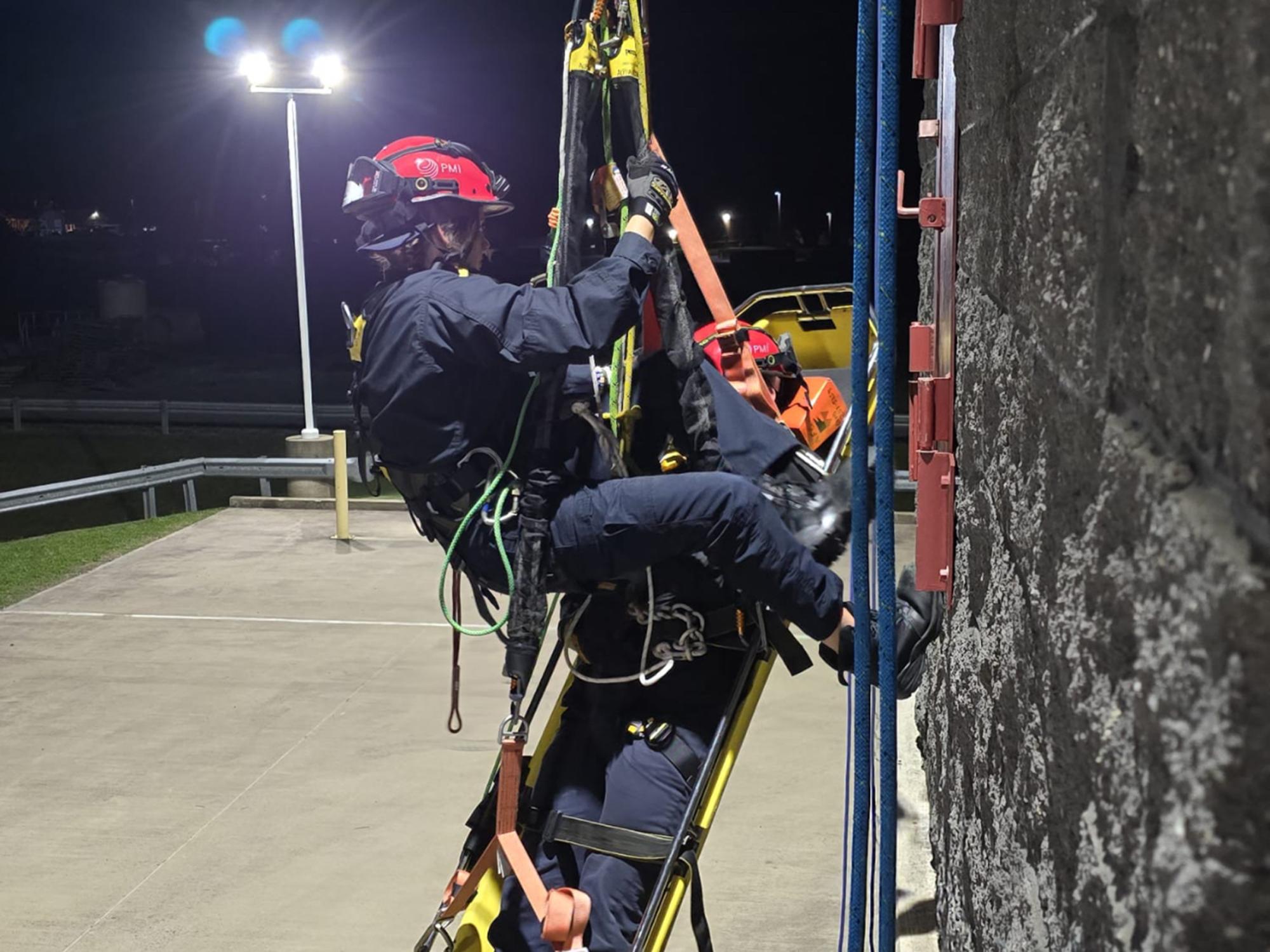 person hanging from a rope bring another person out of a tall building