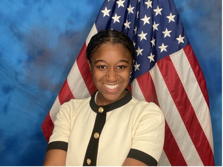 Xiomara Larkin posing for a picture in front of an American flag on a blue background.
