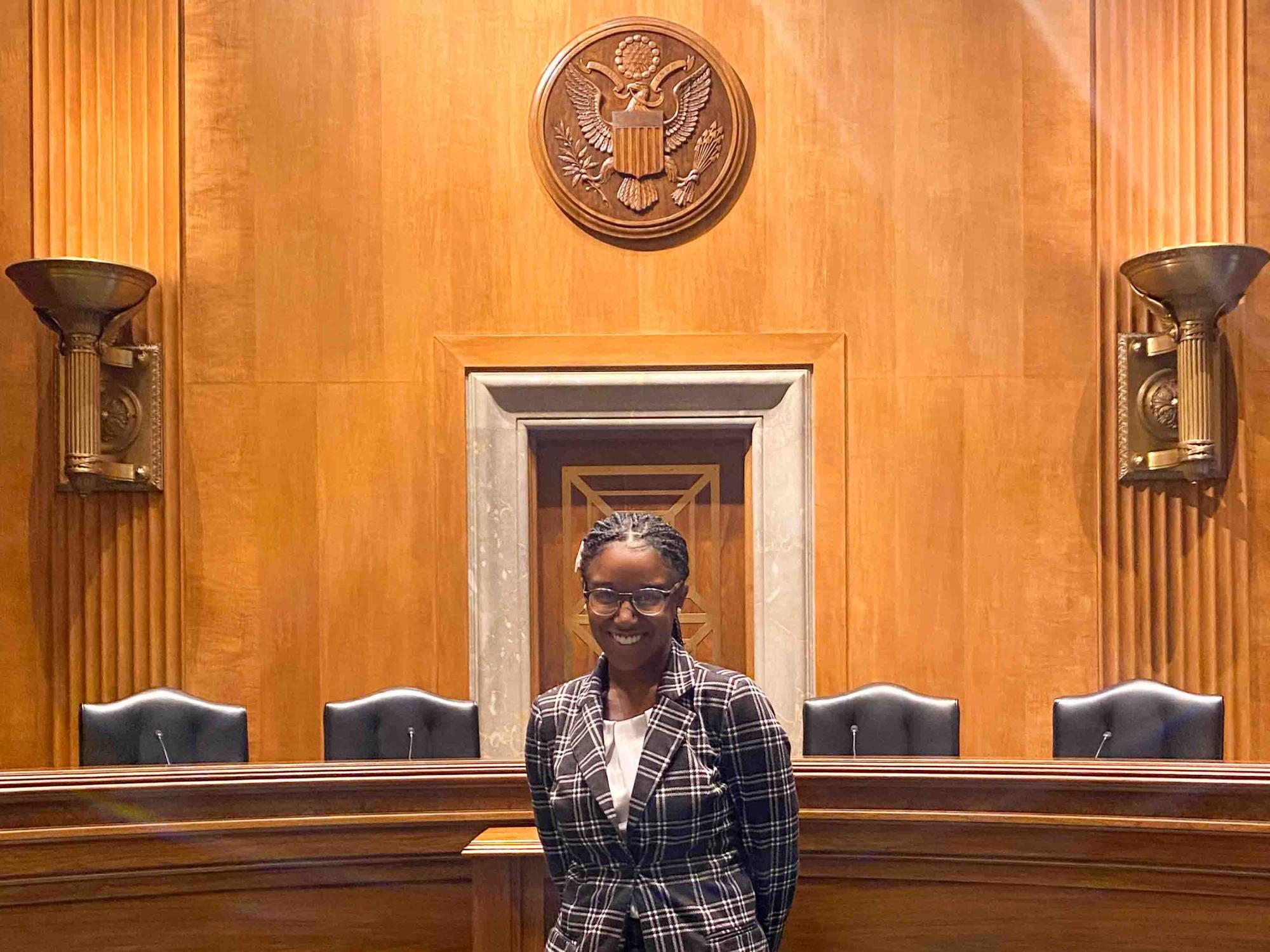 Xiomara Larkin stands in front of four chairs in a committee room in the U.S. Capitol Building.