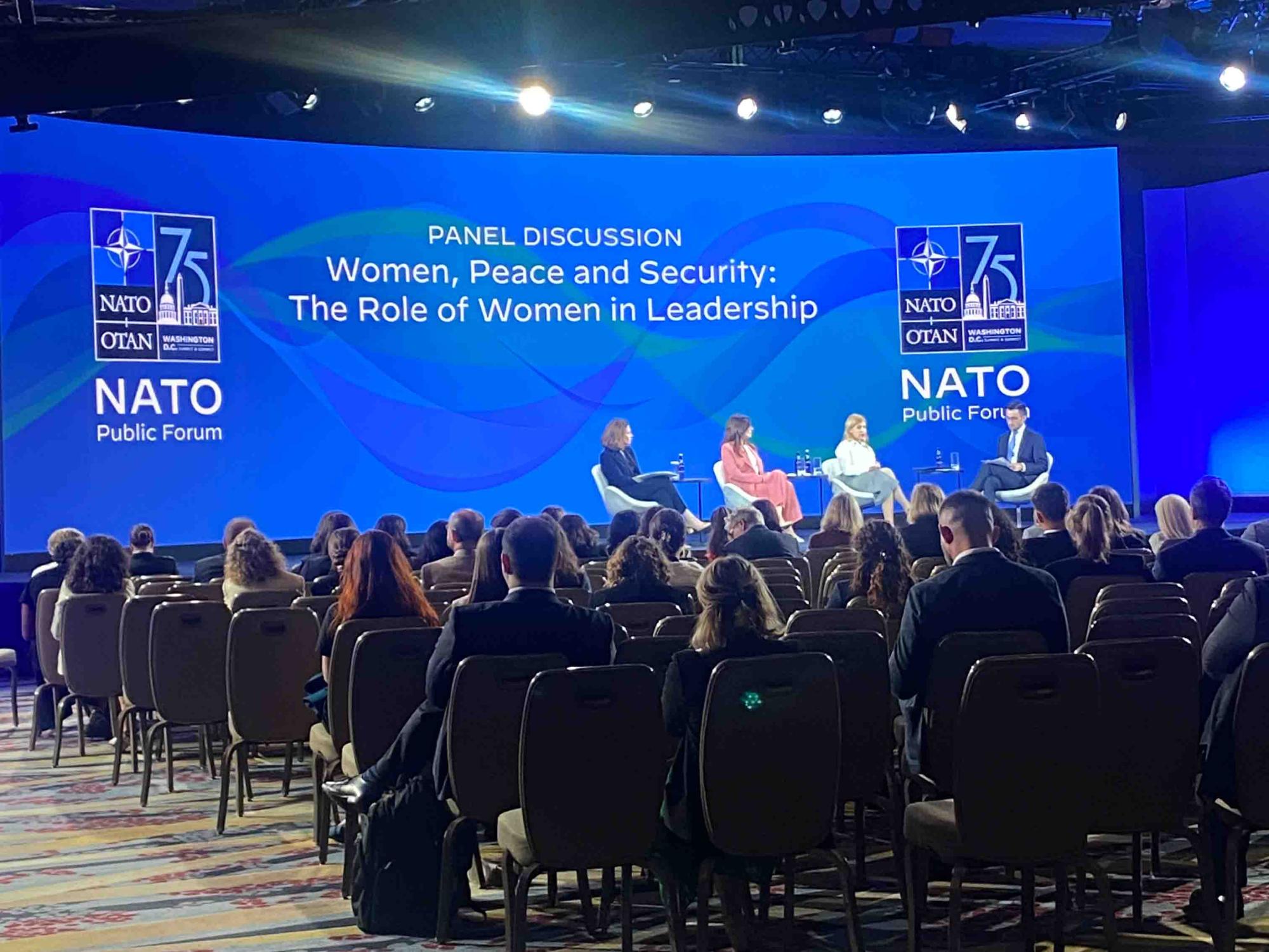 Forum room filled with people watching a panel discussion on “Women, Peace and Security: The Role of Women in Leadership” with three panelists and one moderator sitting on the stage at a NATO Public Forum. 