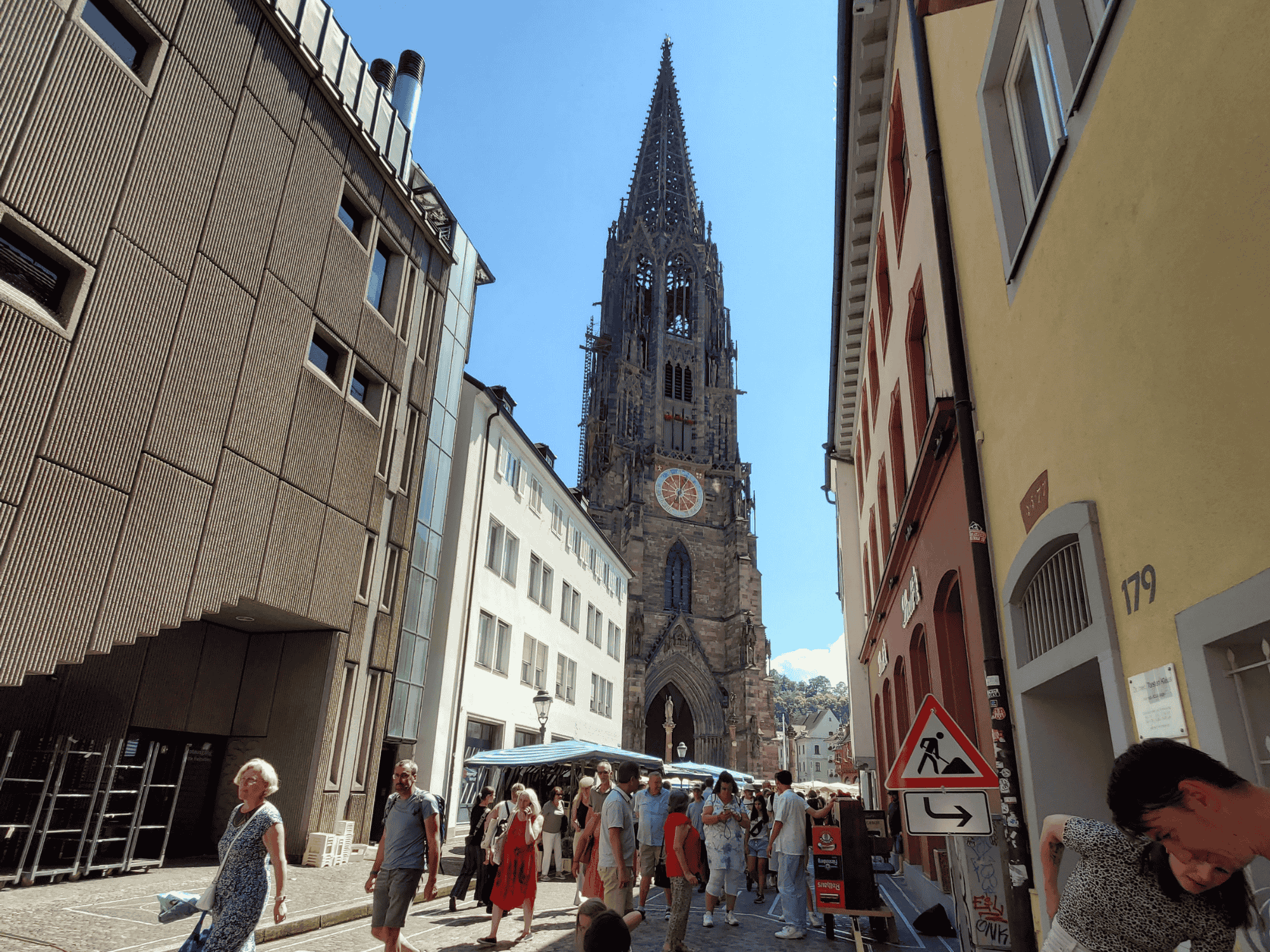 A busy street with a farmer's market in Freiburg, Germany, with the Freiburg cathedral in the background.