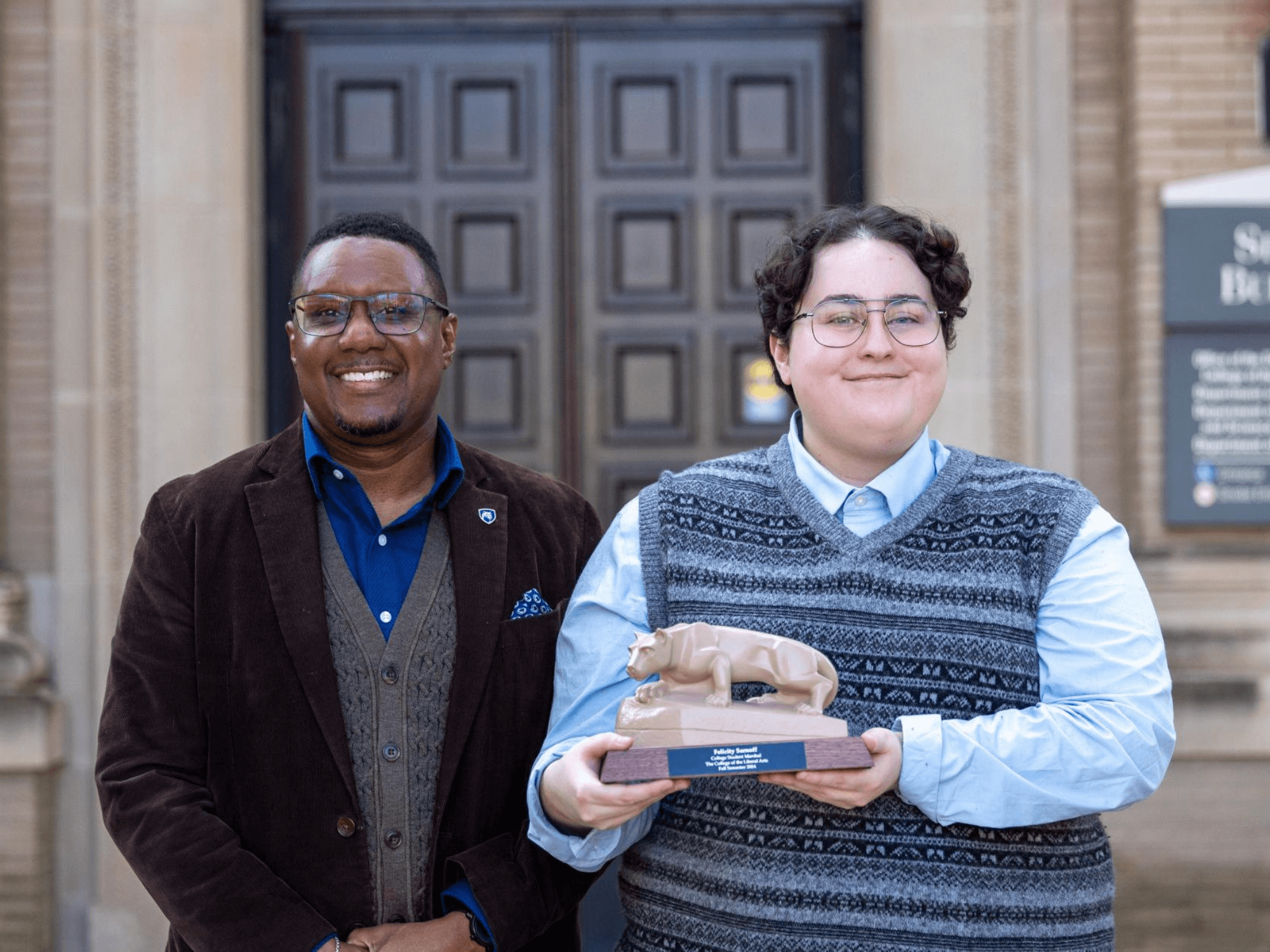 Clarence Lang, Susan Welch Dean of the College of the Liberal Arts (left) stands next to Felicity Sarnoff (right) in front of the north entrance to Sparks Building while Sarnoff holds a mini Nittany Lion statue.