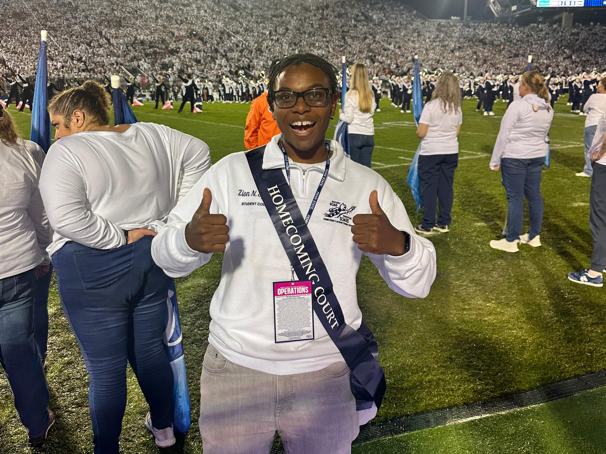Zion Sykes gives two thumbs up and wears a “Homecoming Court” sash while standing on the field at the Penn State Homecoming football game on September 28.