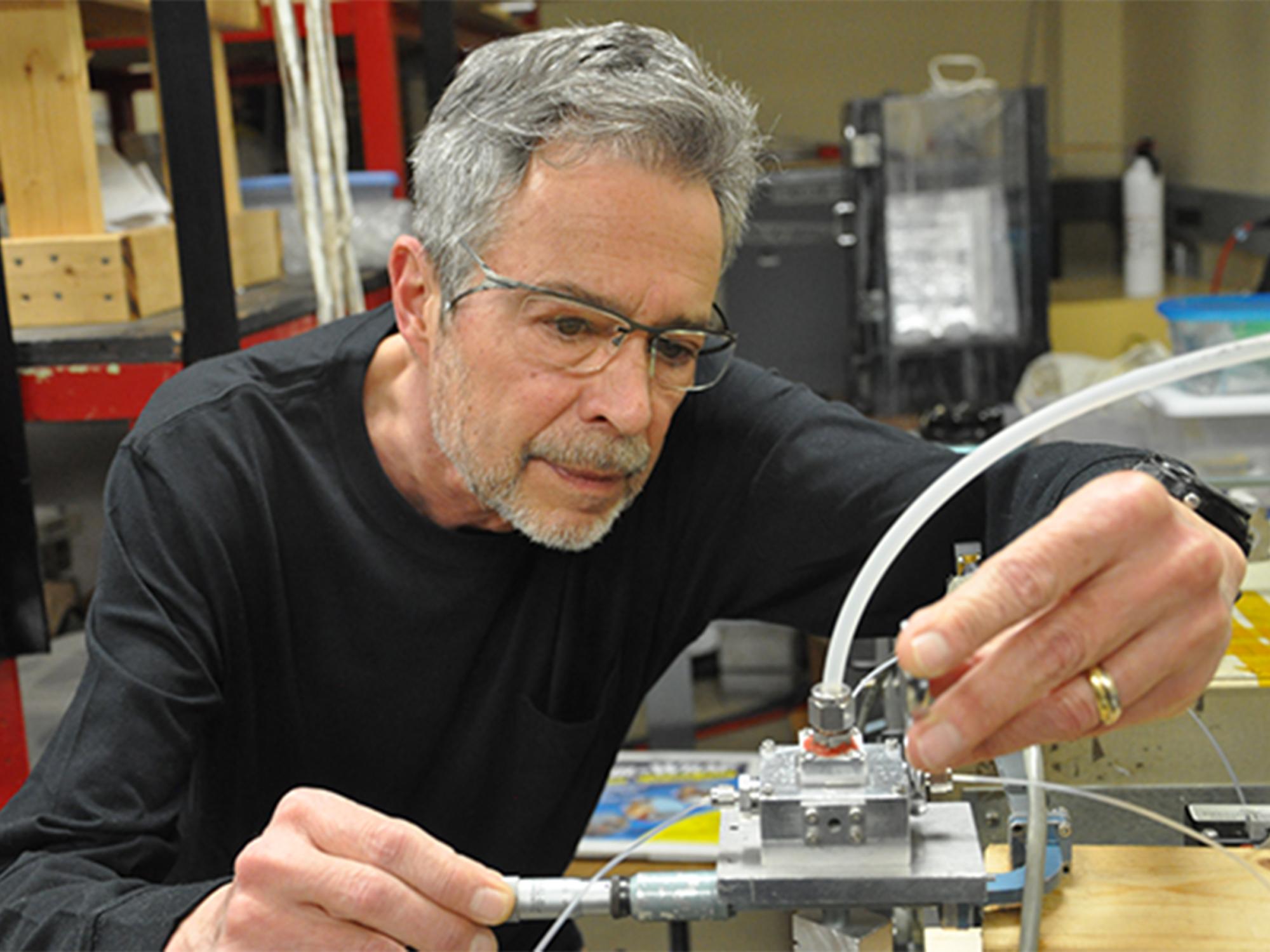 Person with gray hair and glasses touches metal box.