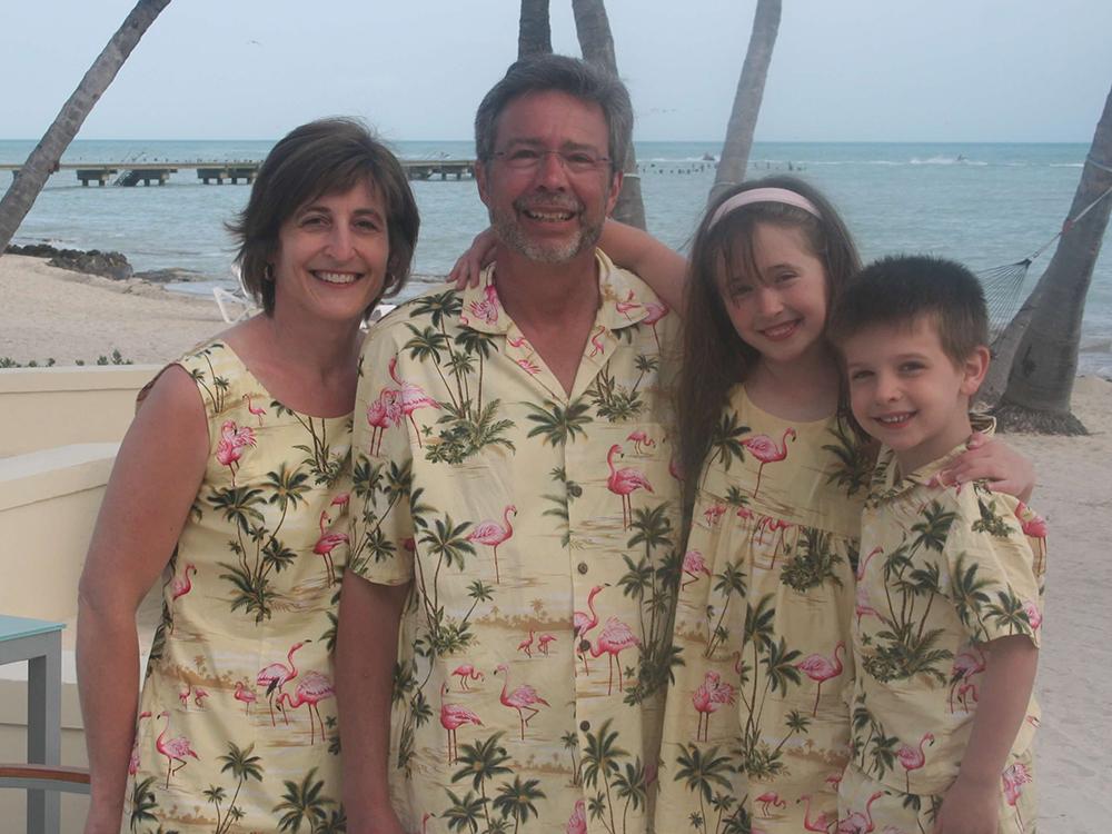 A family portrait of two adults and two kids posing at a beachfront.