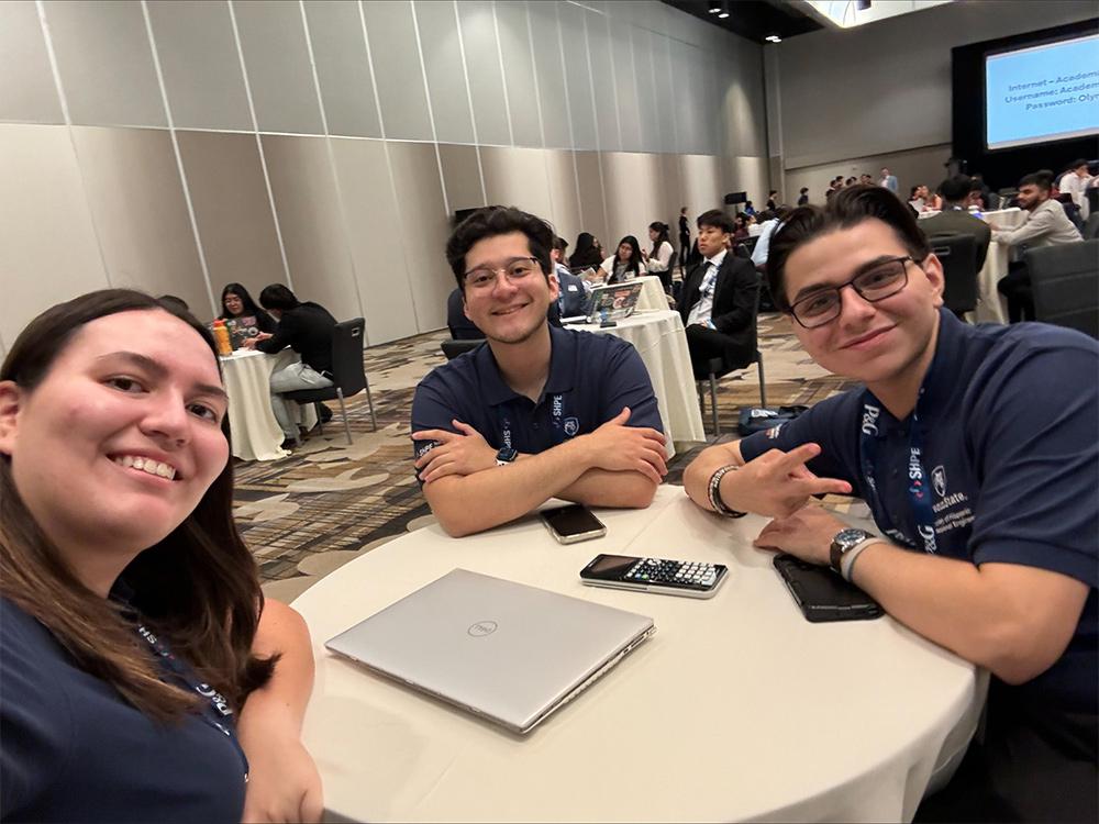 three students pose around a table at a conference