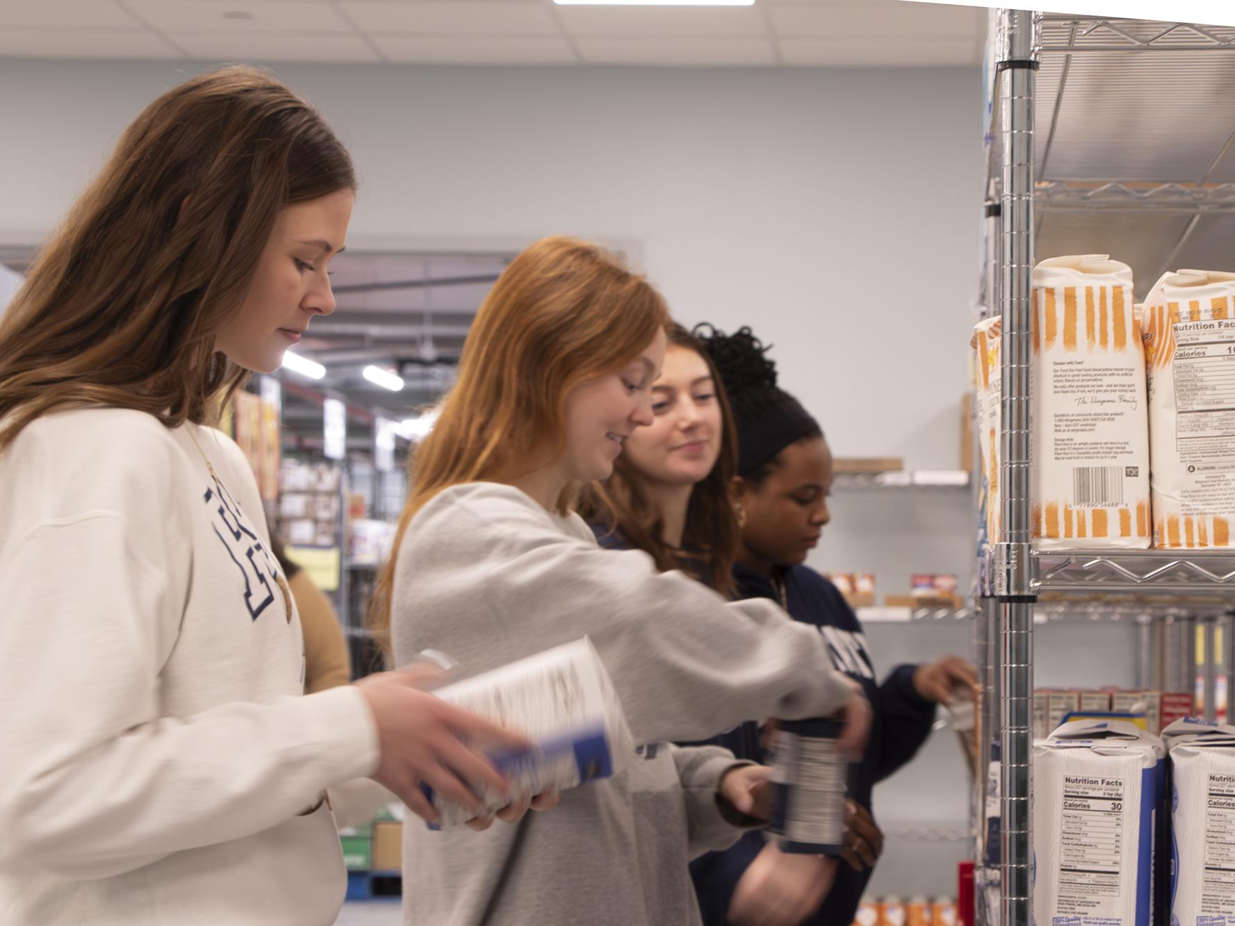 Four students organizing food items on pantry shelves at the State College Food Bank