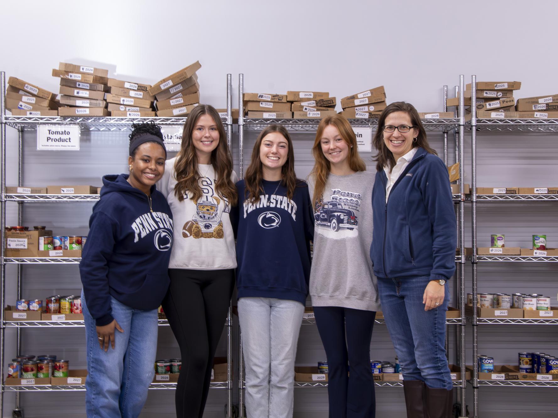 Four students standing in the food organization area of the State College Food Bank with assistant teaching professor of biobehavior health, Danielle Rhubart (far right).