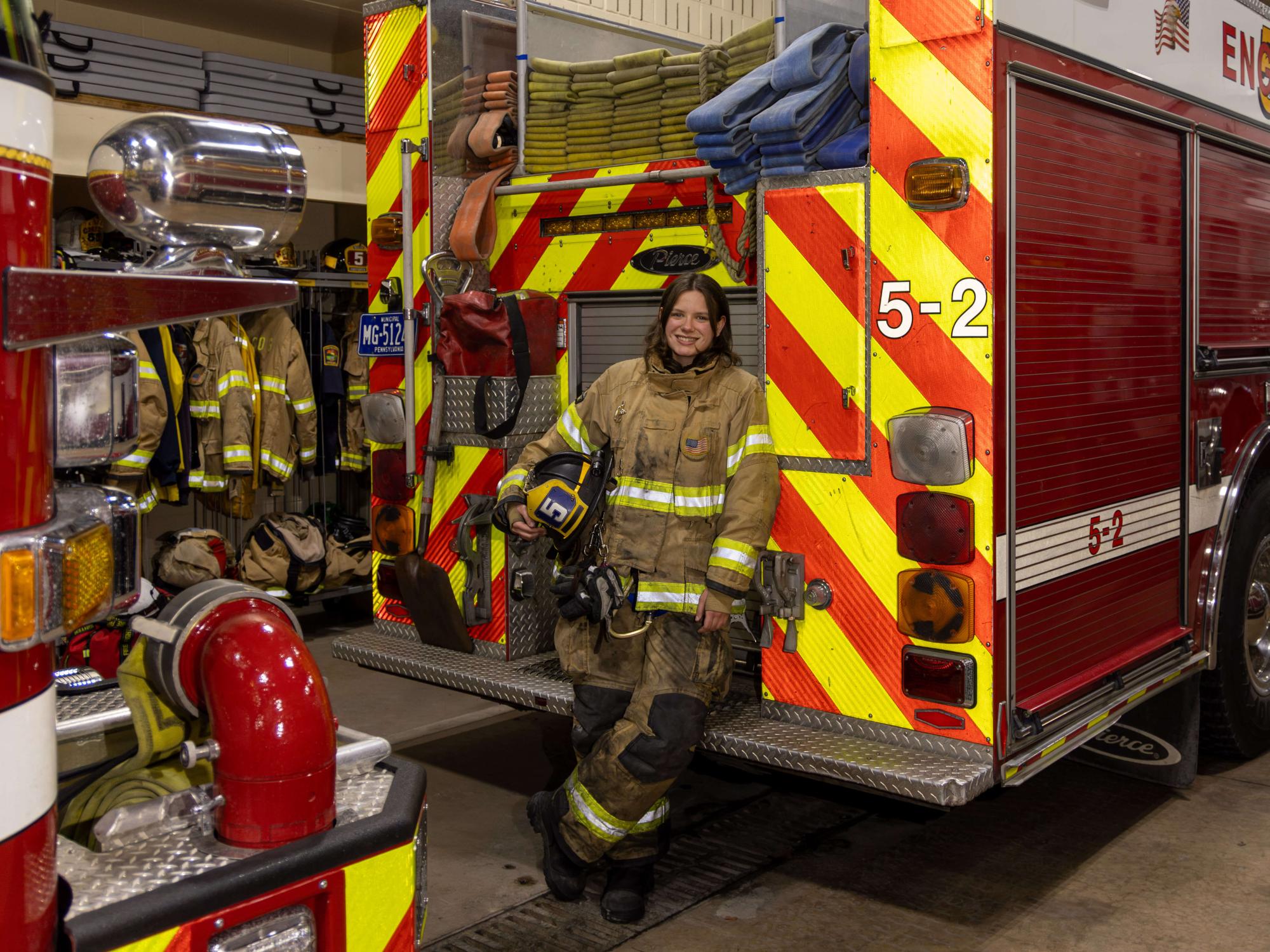 Kara Stover, a Penn State student and volunteer firefighter, leans against the back of a fire engine while wearing her turnout gear inside the Alpha Fire Station in State College, Pennsylvania.