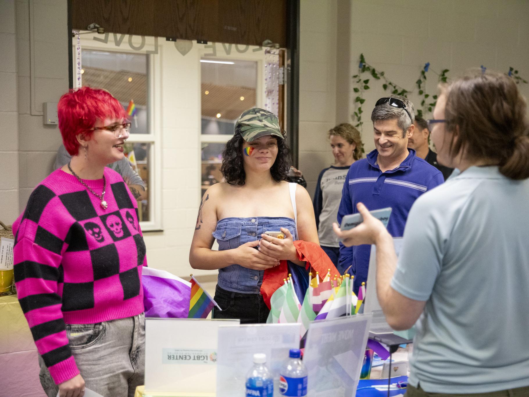 Two students and a faculty member stand at a table with pride flags.