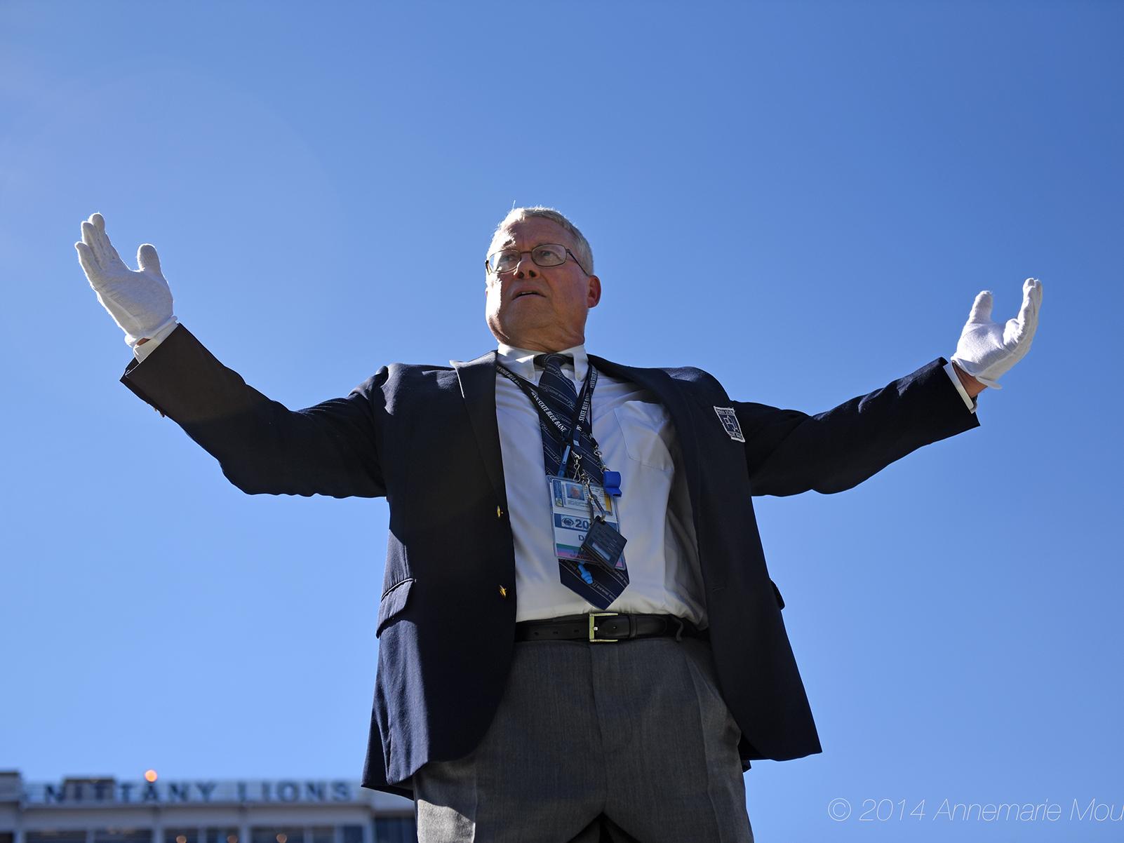O. Richard Bundy stands on a ladder in front of a blue sky with the Beaver Stadium press box visible in the background.