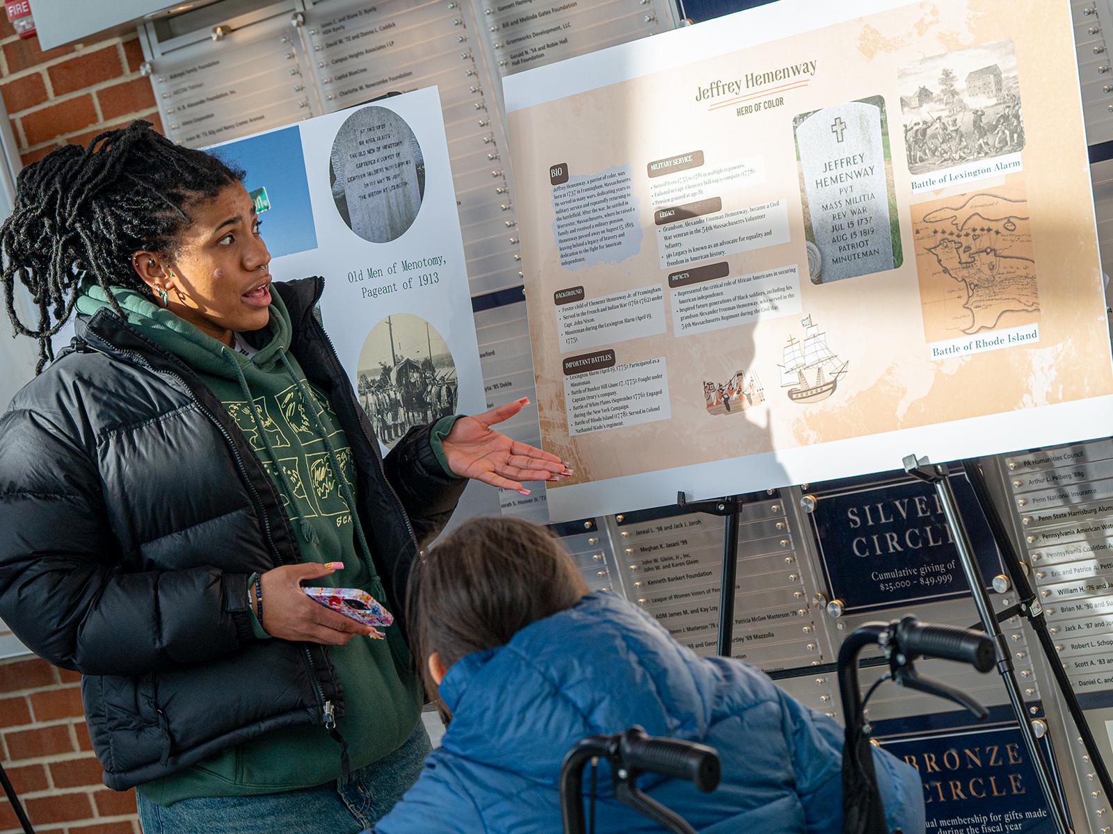 A student explains her research poster to another student