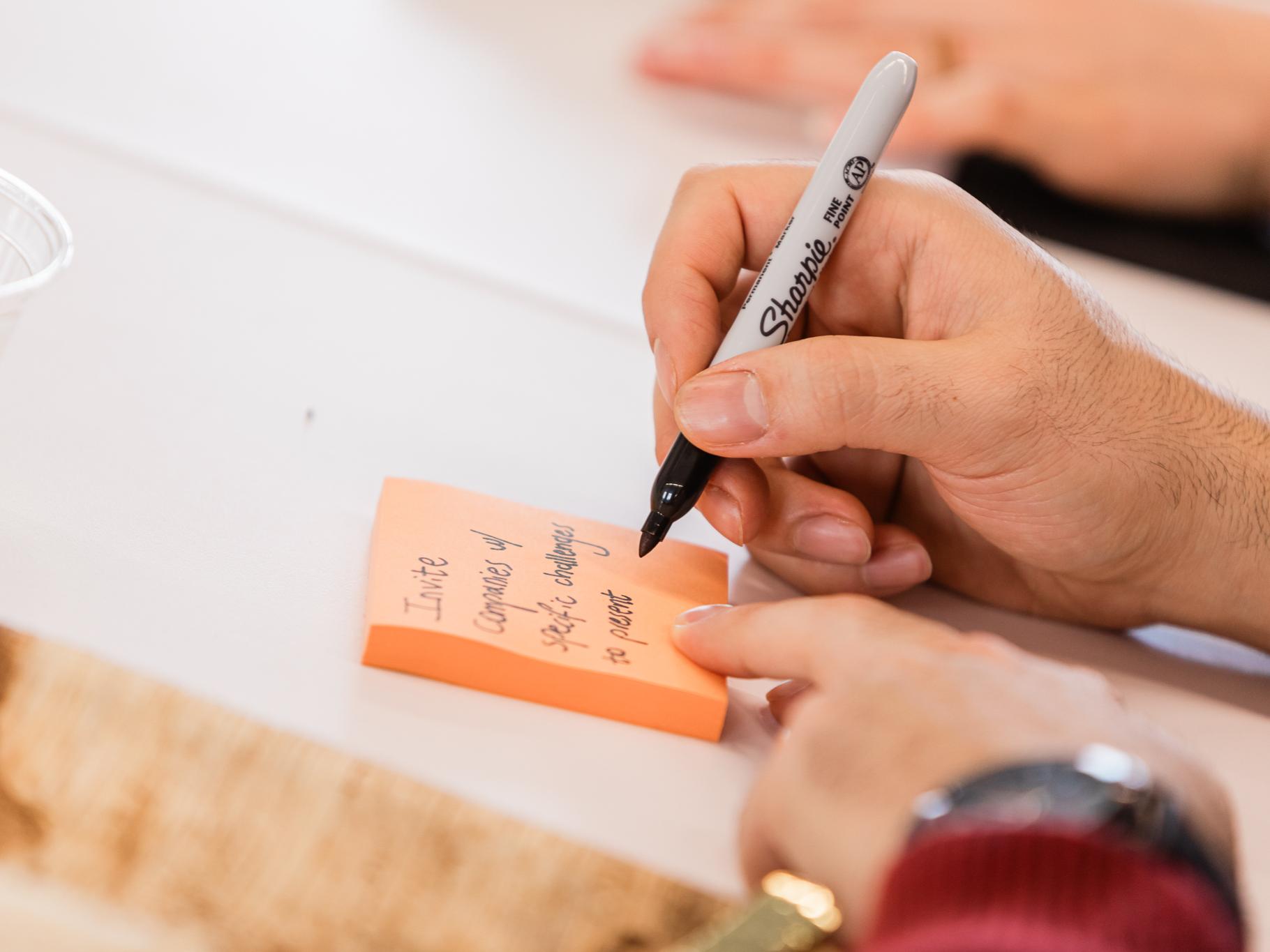 A person writes on a stick note with a sharpie marker