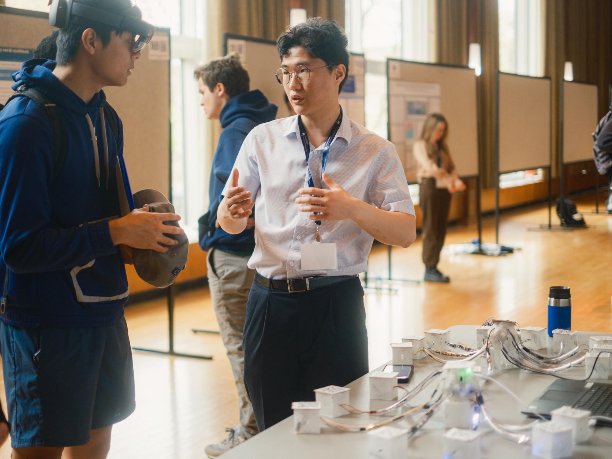Student explaining research to another standing in front of table with props