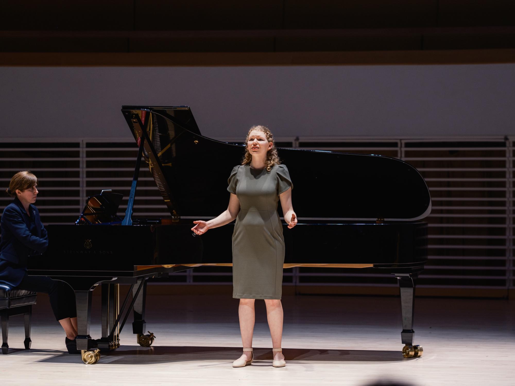 Student singing in front of piano on stage