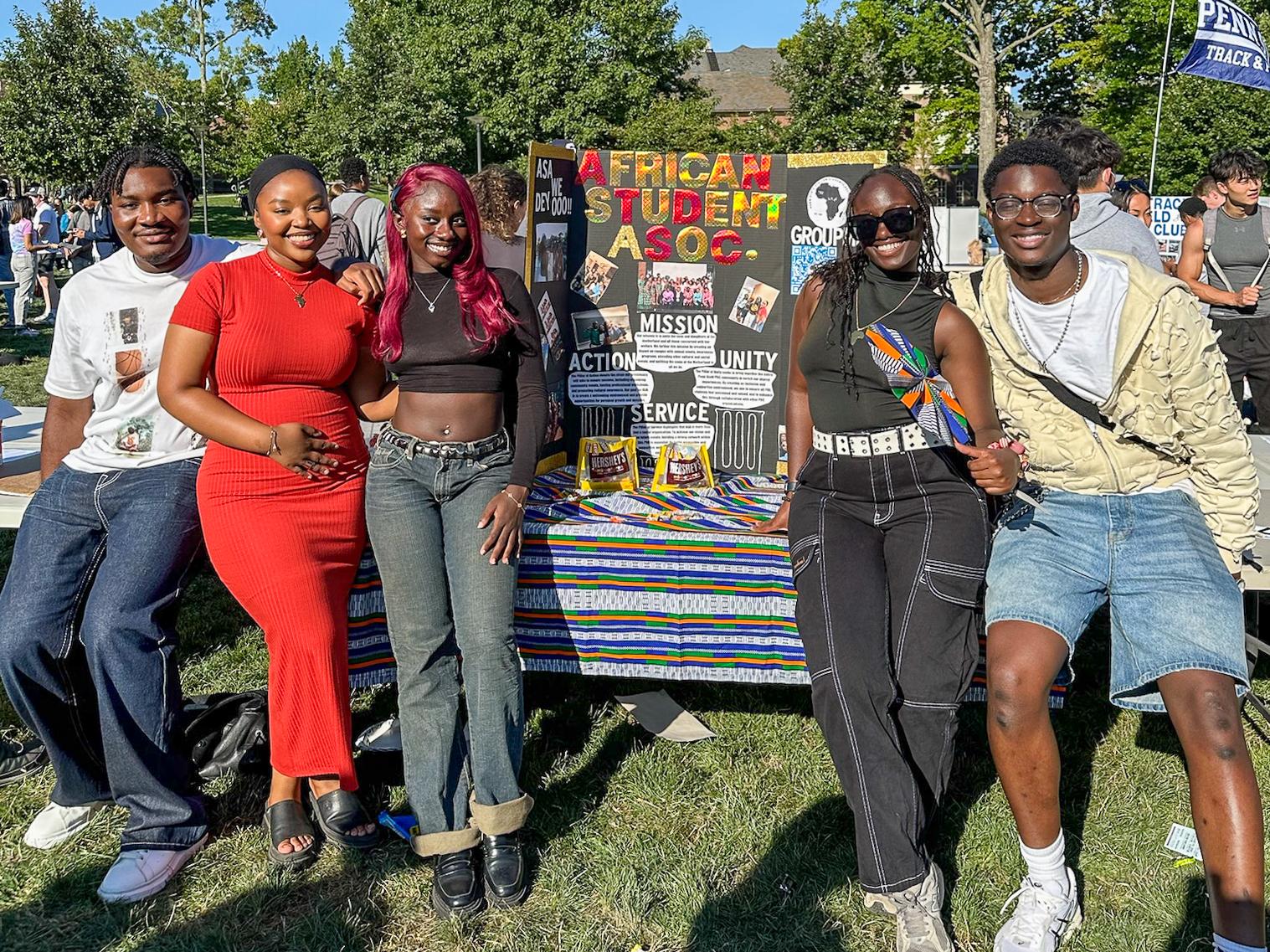 A group of five students smile while sitting in front of a decorated poster.