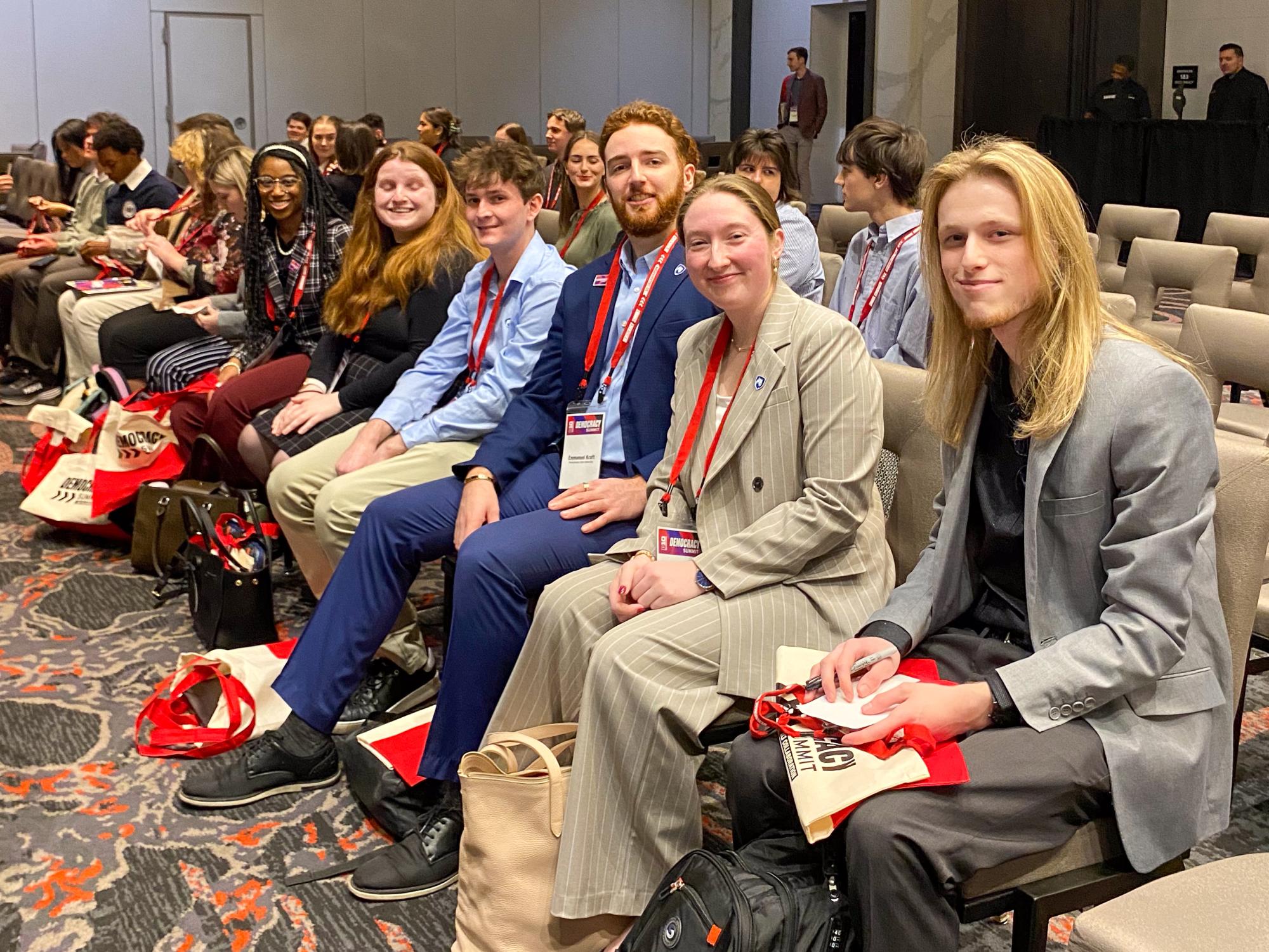 Penn State students sitting on chairs in a row, in a large venue, smiling at the camera.