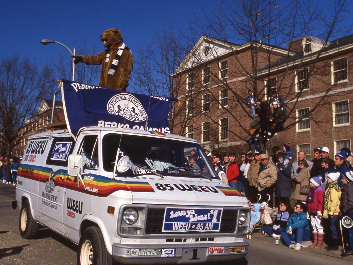 The Nittany Lion rides on top of a white van during a parade