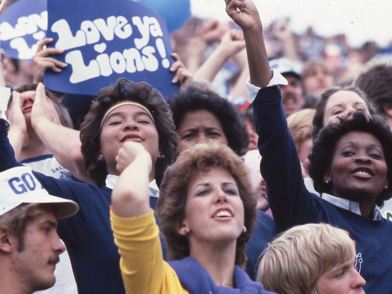 Fans cheer on the Penn State football team, with one holding a sign that reads "Love Ya Lions"