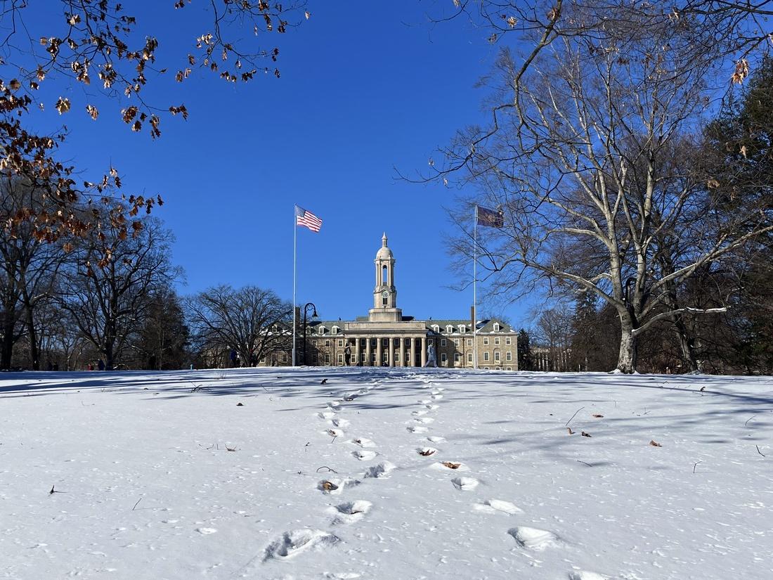 A faraway picture of Old Main with a blue sky behind it and several paths of footprints in the snow leading to it