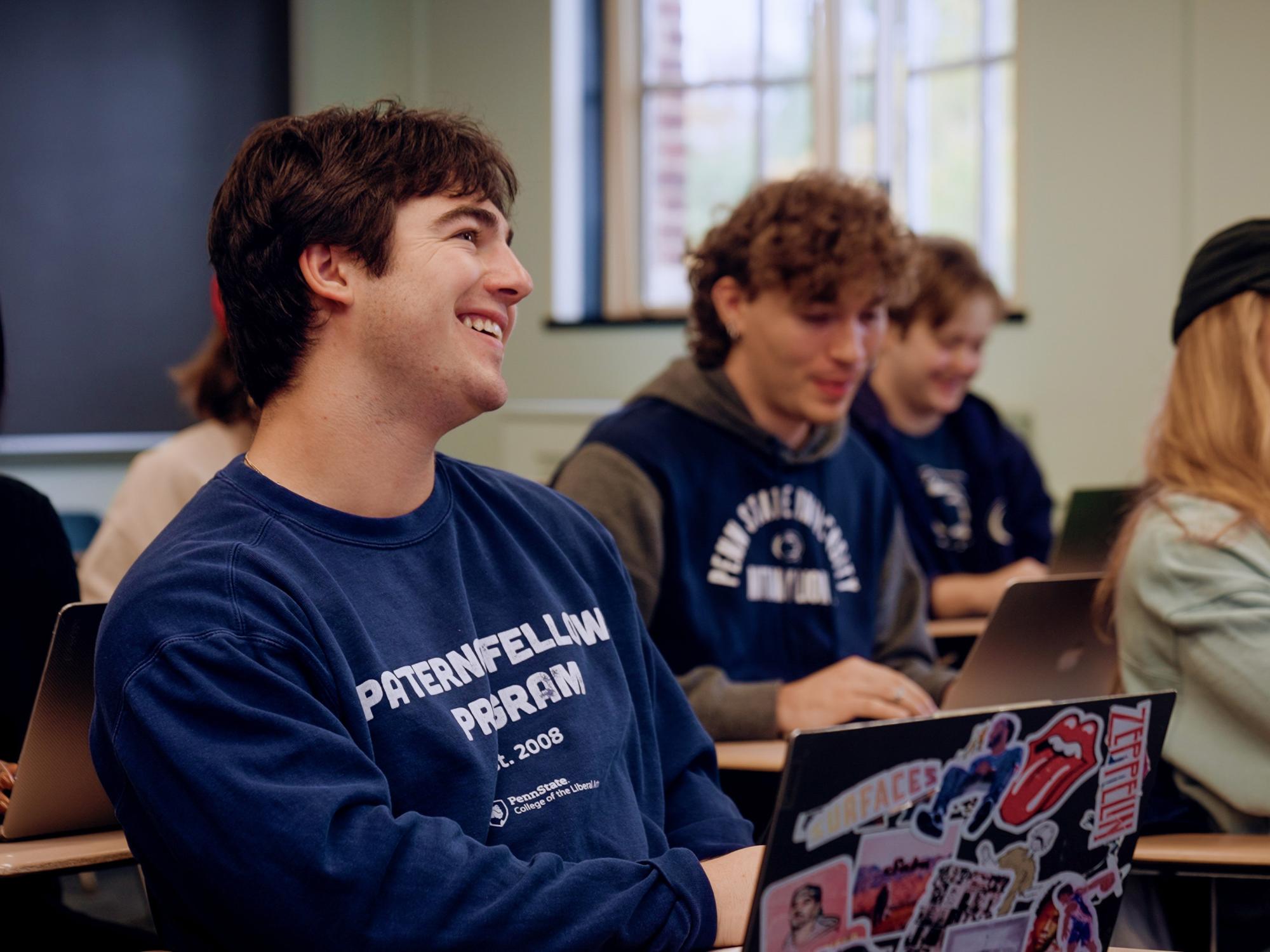 Owen Perry sits at a desk with his laptop open in front of him in a “Paterno Fellows Program” sweatshirt.
