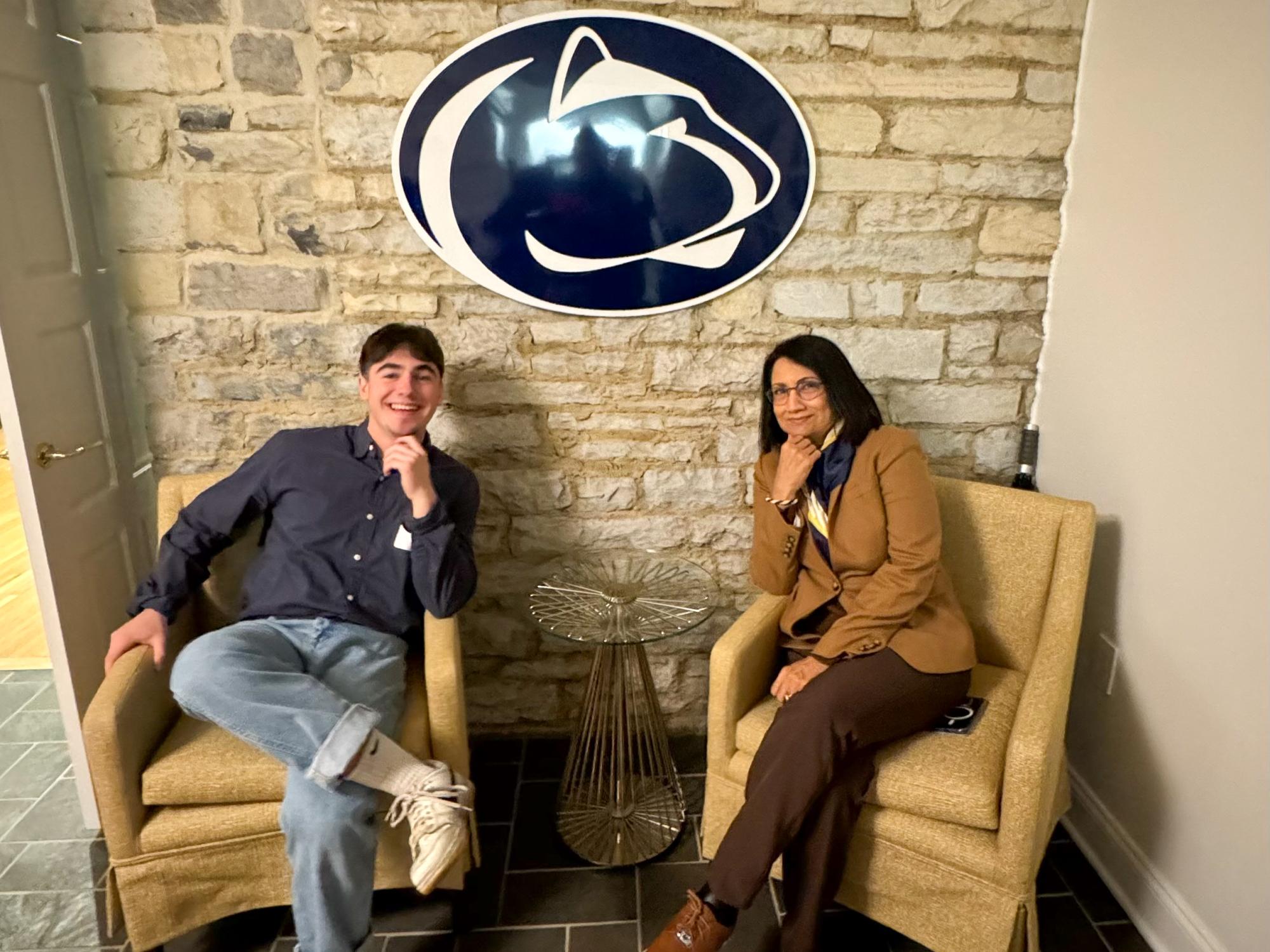 Owen Perry sits next to Penn State President Neeli Bendapudi with the Penn State Athletics logo on the wall behind them.